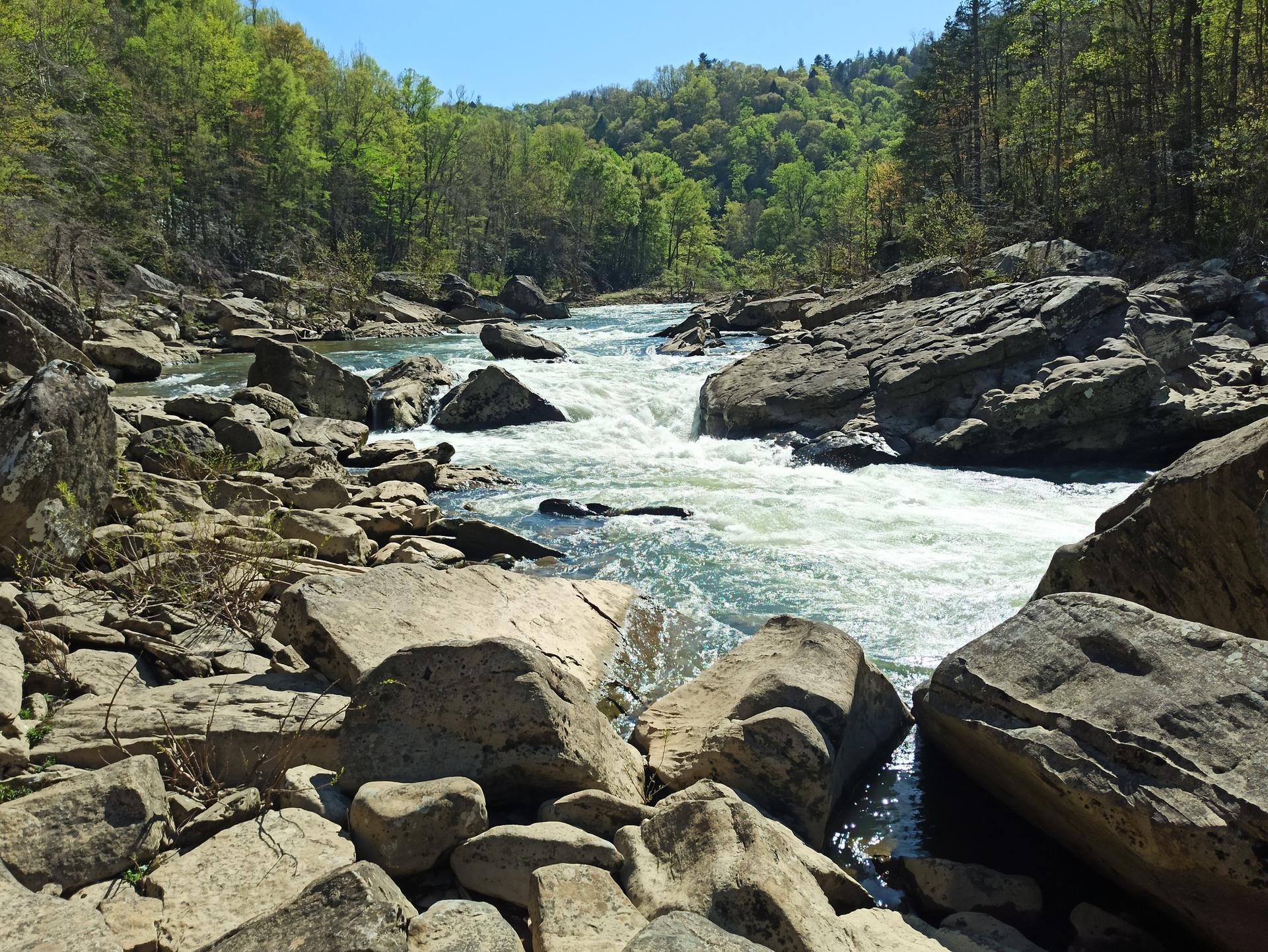 Sunny view of a rushing river flowing over large rocks.