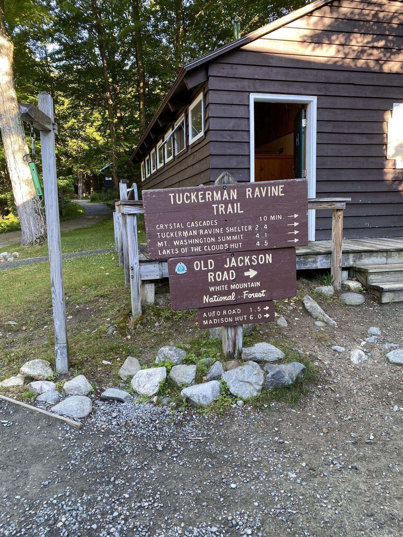Brown cabin and wooden trail signs in a sunny, forested area.