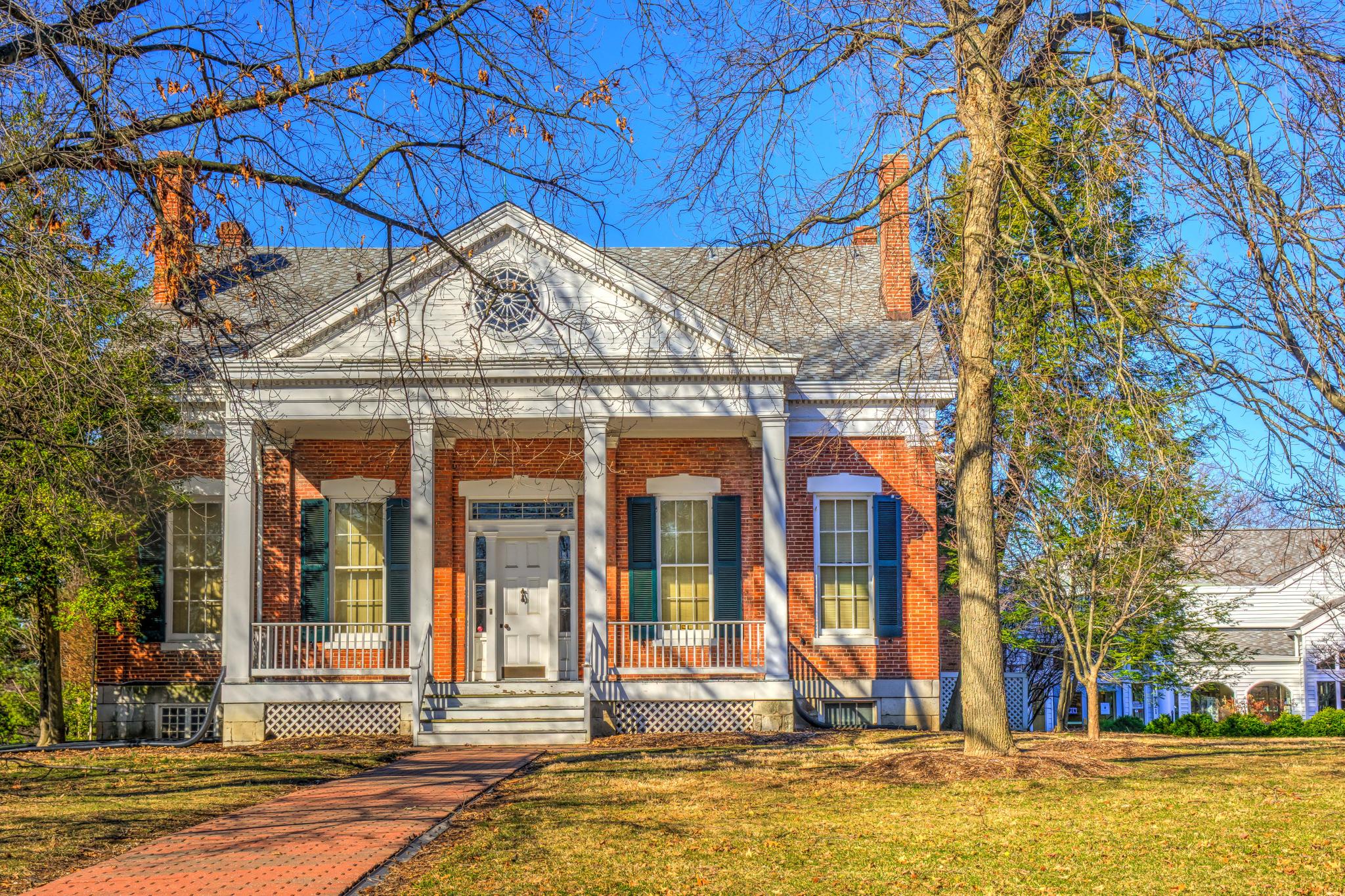 Sunny view of a large brick house with a white columned porch and bare trees.