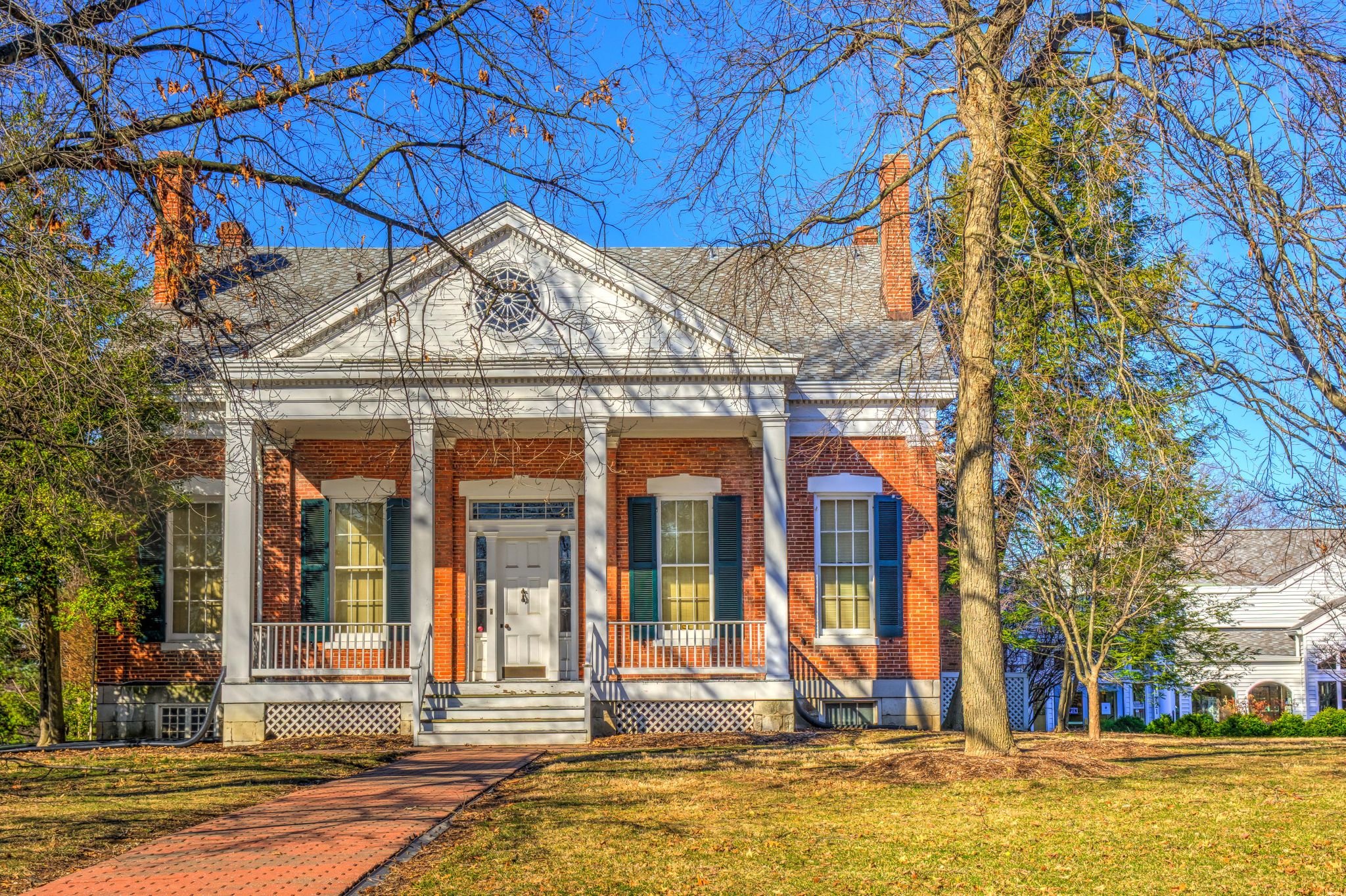 Sunny view of a large brick house with a white columned porch and bare trees. - Hawk Ridge Trail