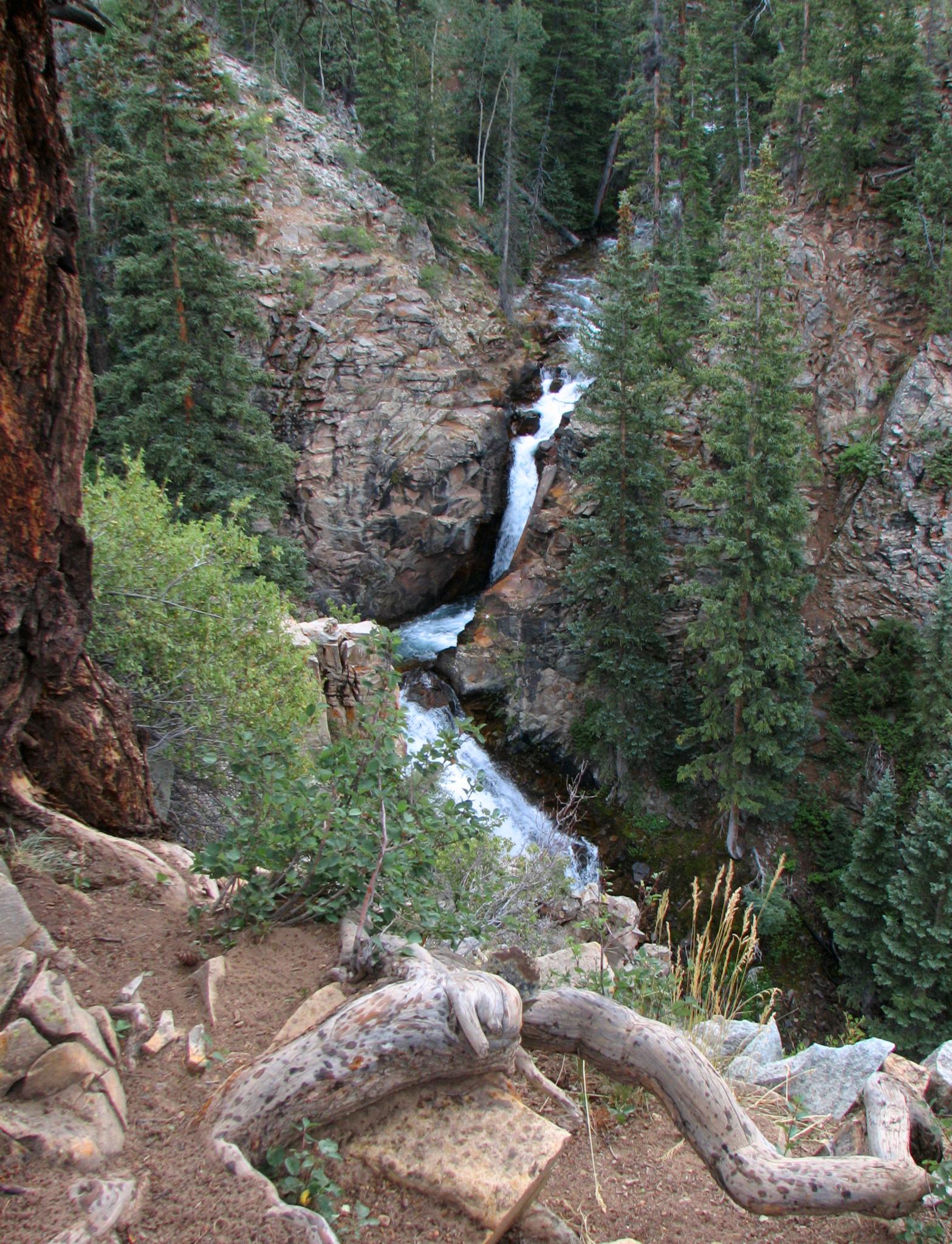 A multi-tiered waterfall cascades down a rocky gorge surrounded by dense forest.
