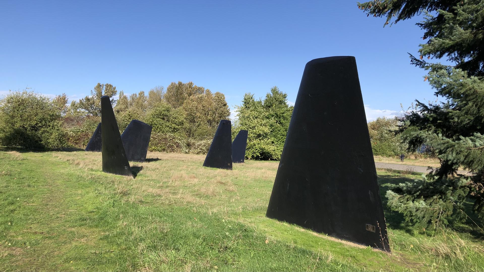 Several large black triangular sculptures stand in a sunny grassy field.