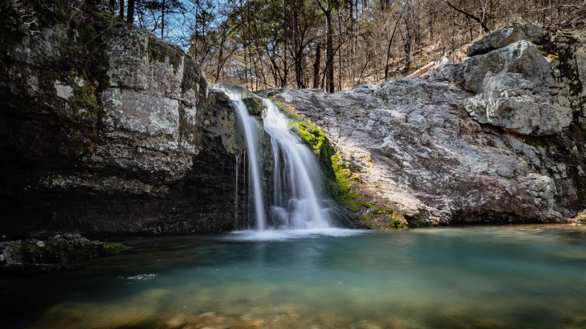 Scenic waterfall flowing into a tranquil pool amidst rocky forest. - Falls Branch Trail