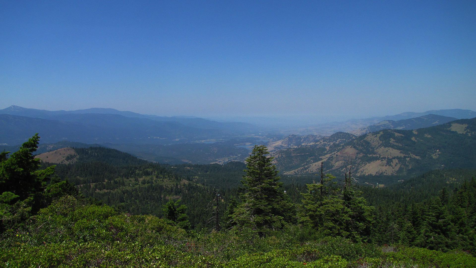 Expansive view of rolling forested mountains and a distant valley under a clear sky.