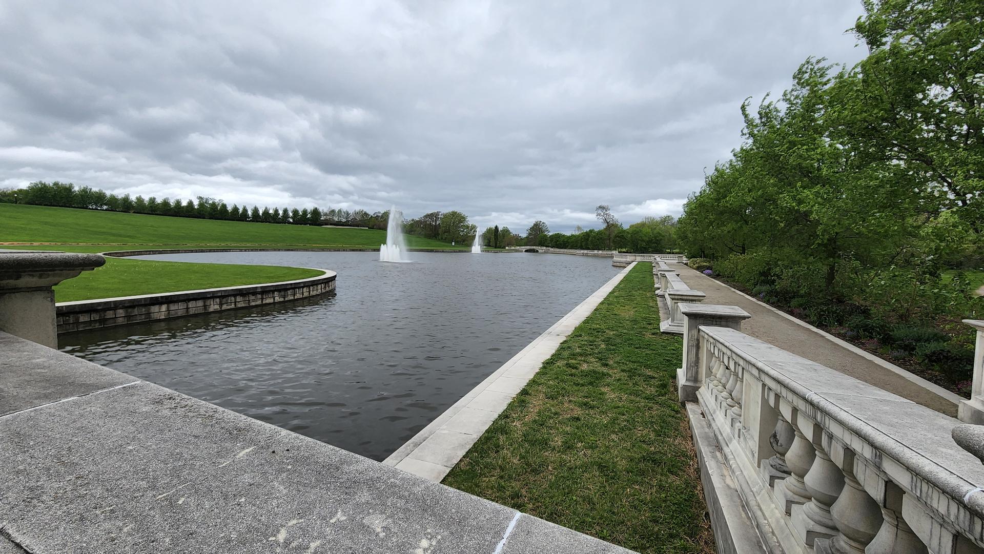 Overcast day over a large pond with two fountains and manicured lawns.