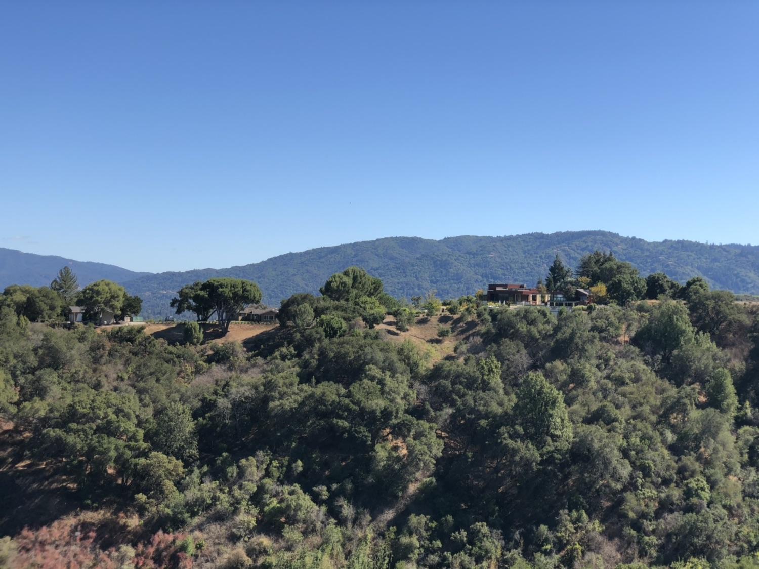 Green forested hills with houses on a distant ridge under a clear blue sky.