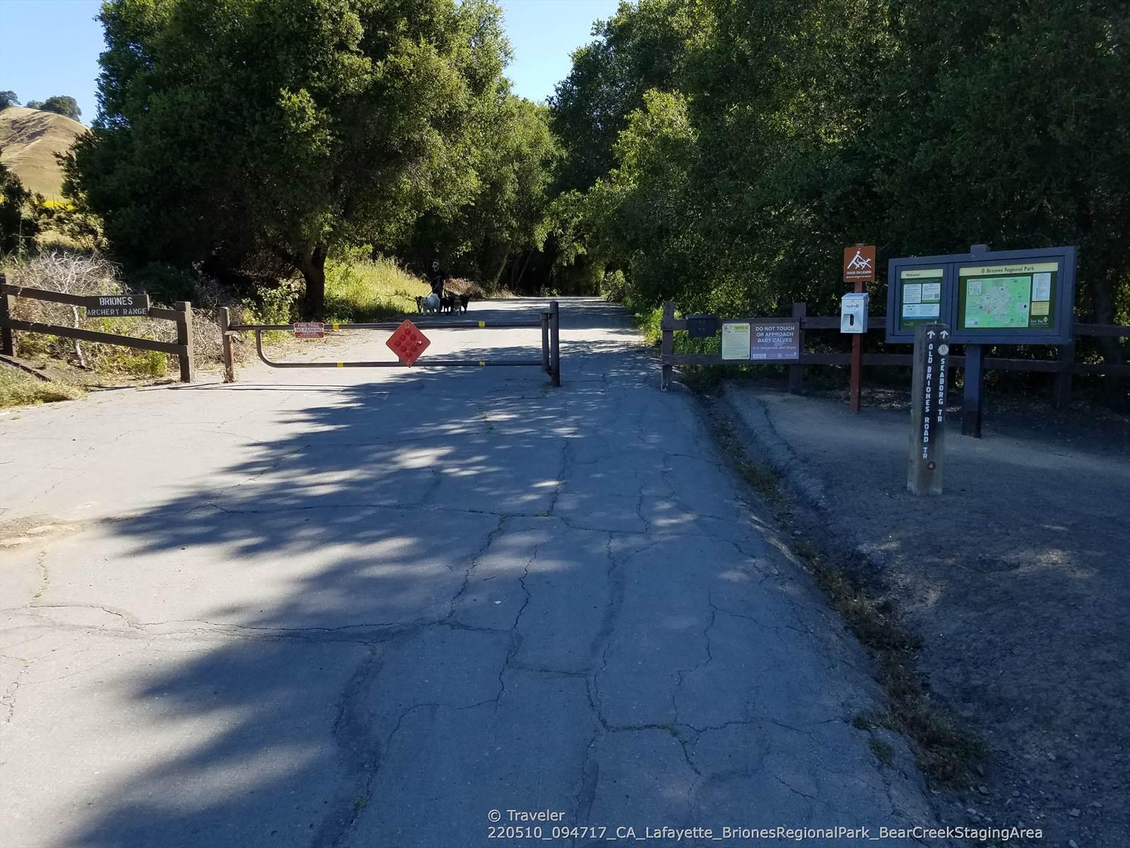 Paved road leading to a park entrance with information signs and trees.