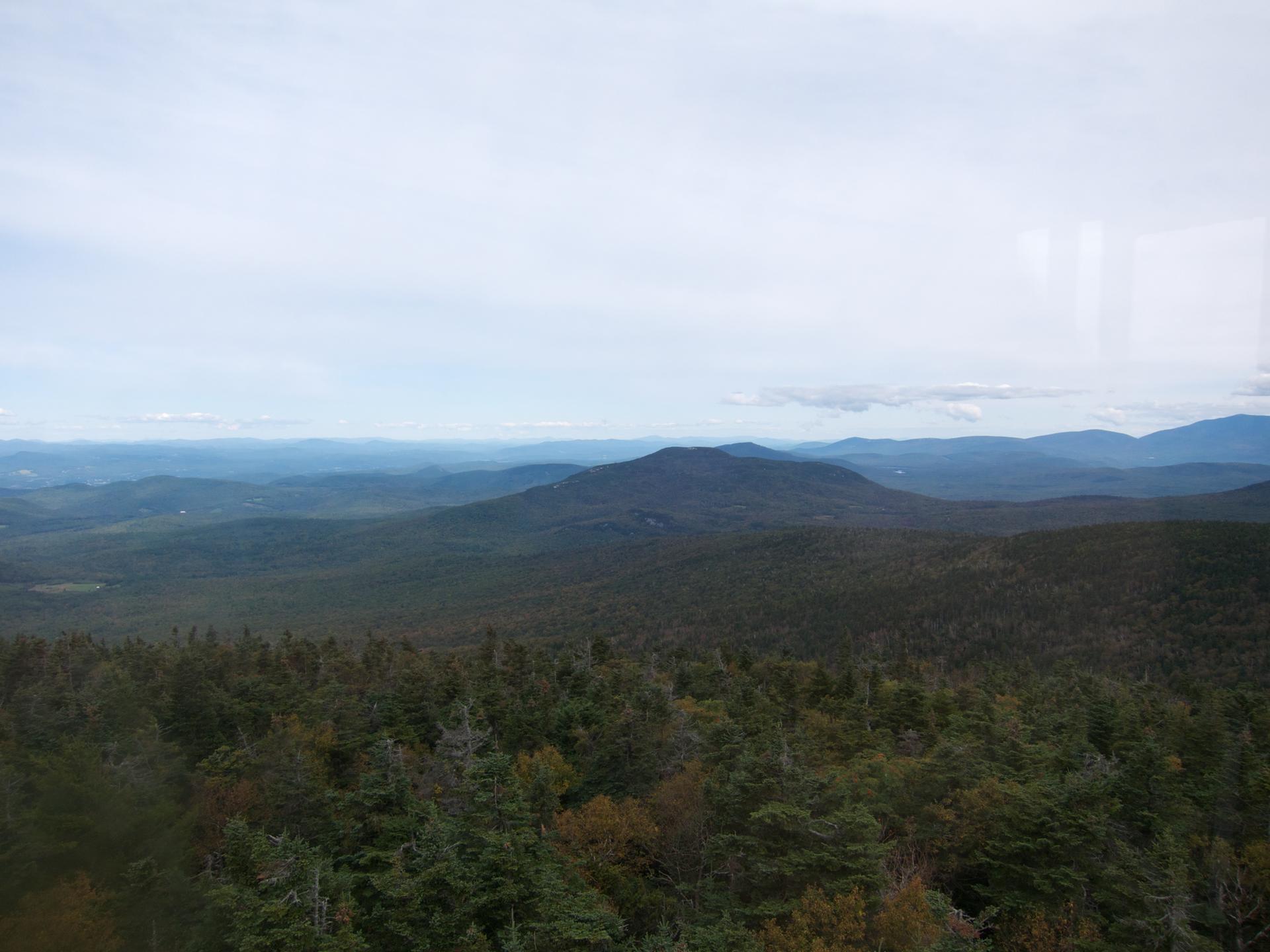 Expansive view of rolling forested mountains under a bright, overcast sky.