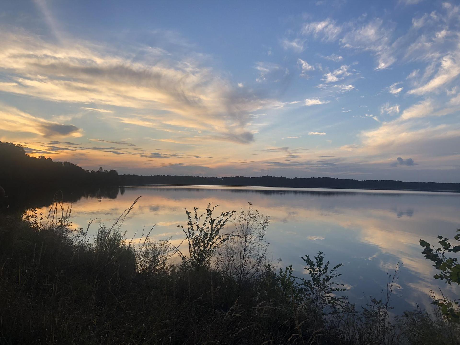 Serene lake reflecting a vibrant sunset sky with silhouetted trees.