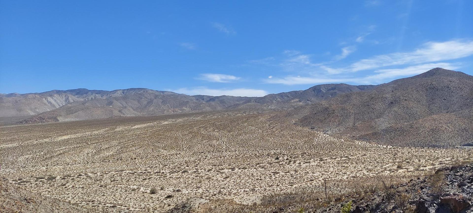 Expansive desert valley with scrub brush and distant mountains under a blue sky.