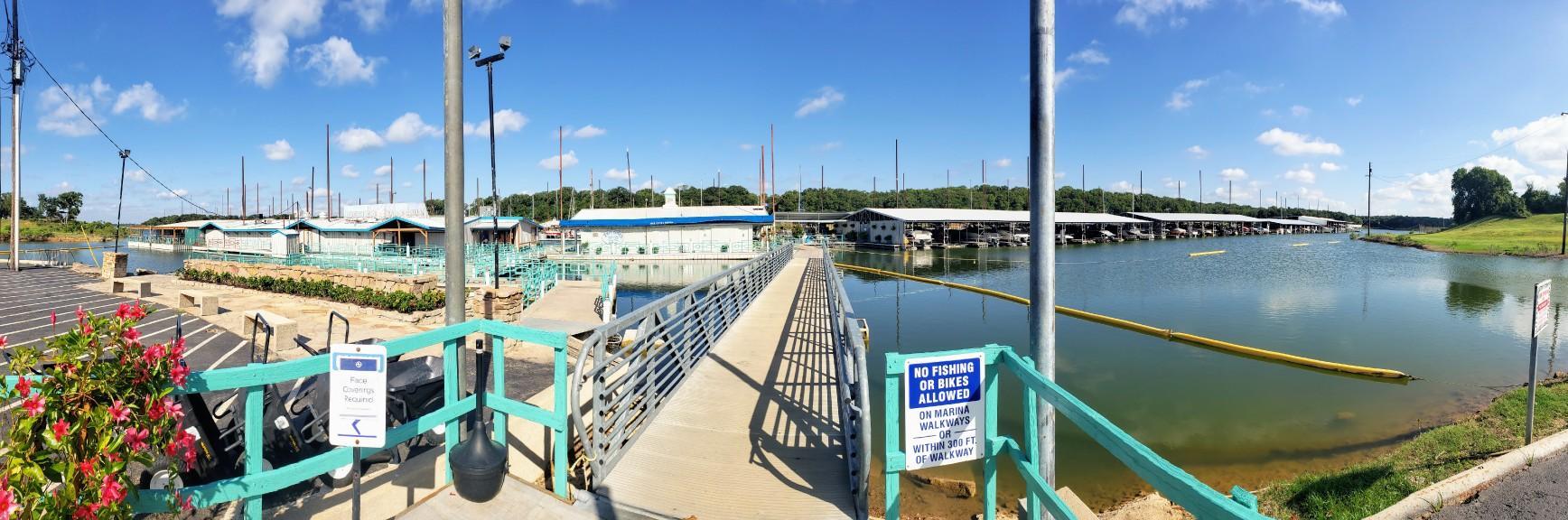 A marina with covered boat slips, a long walkway, and a bright blue sky.