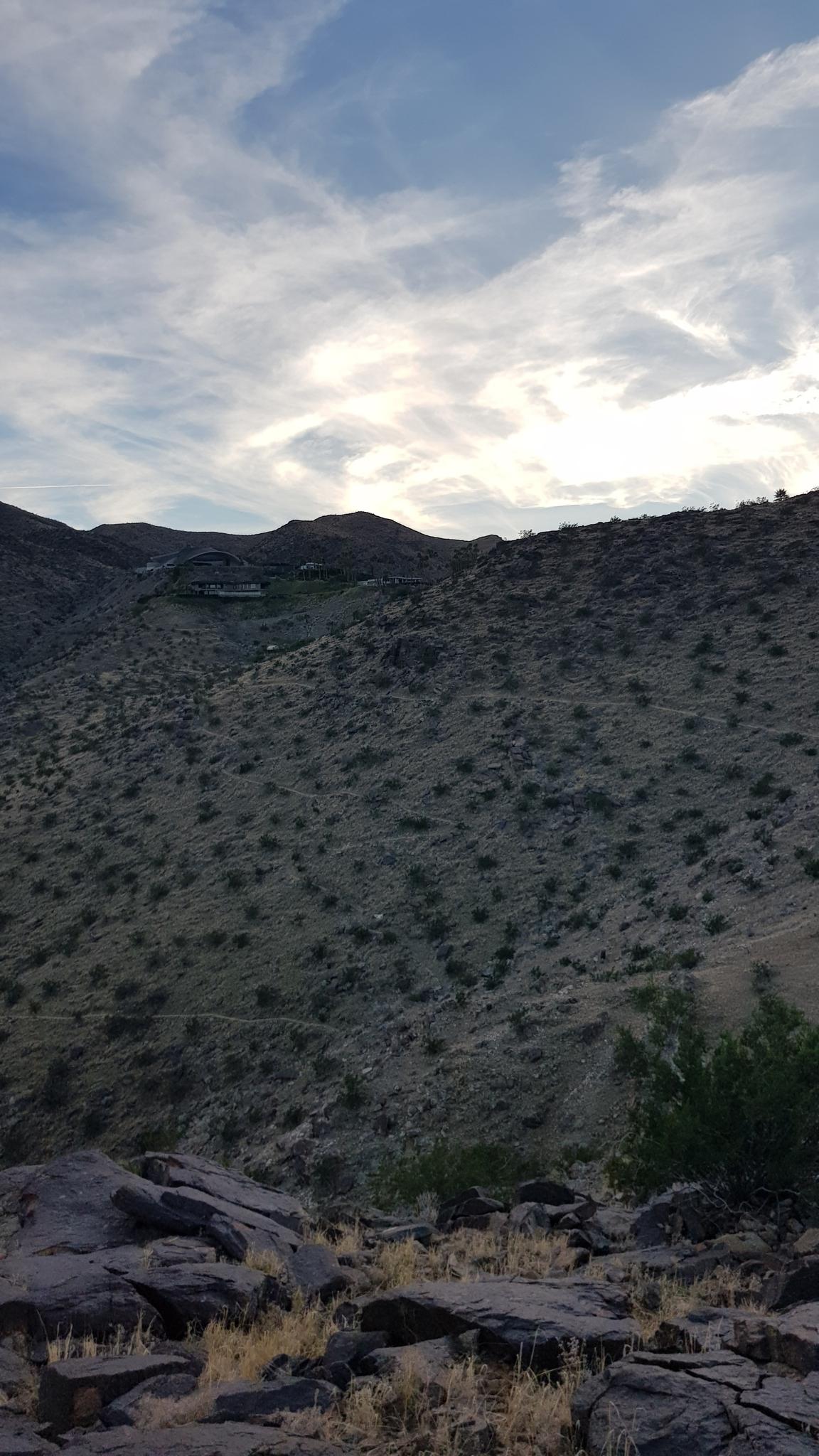 Arid desert mountainside under a cloudy sky with sparse vegetation.