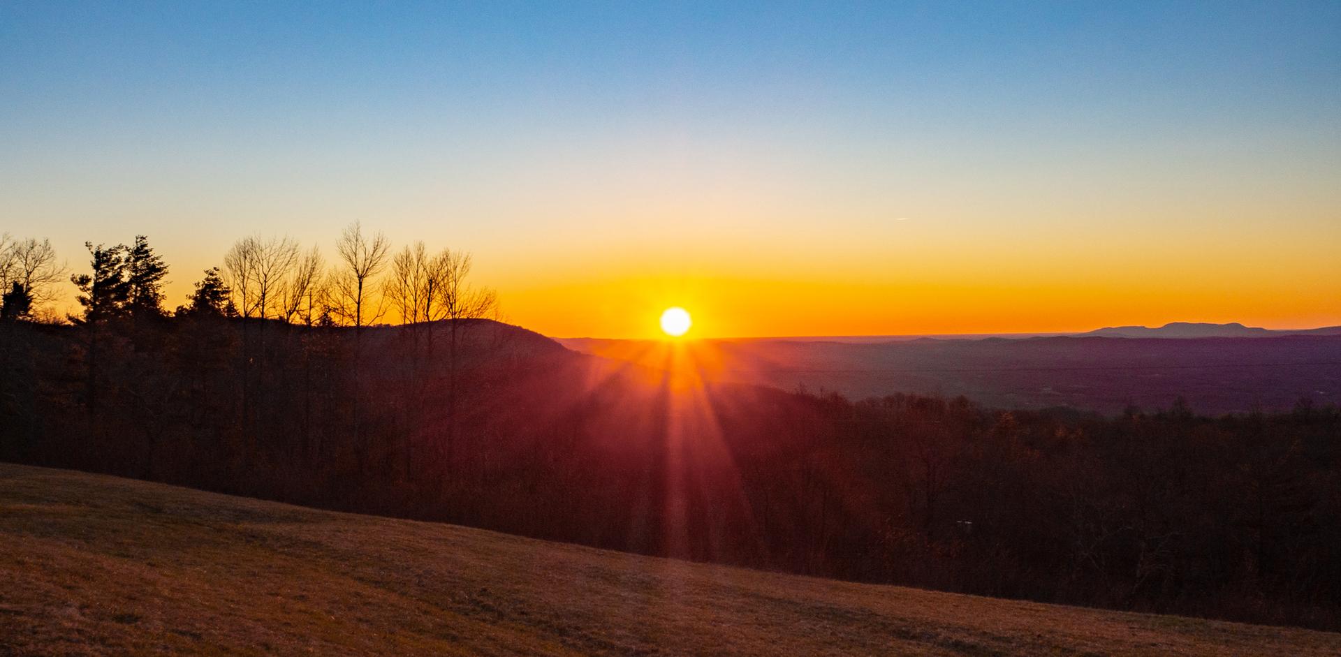 Vibrant sunset over a hilly landscape, with bright sun rays.