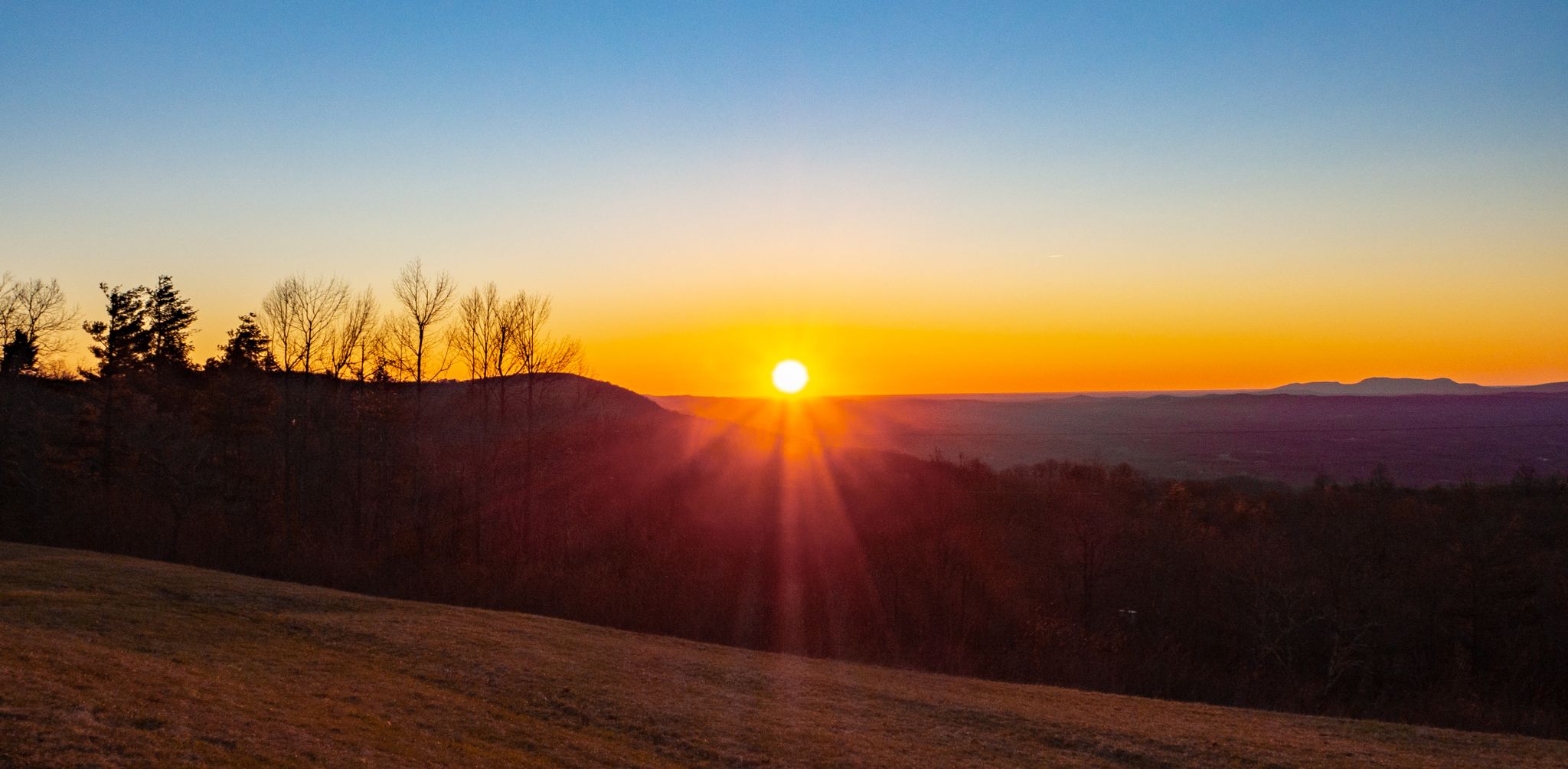 Vibrant sunset over a hilly landscape, with bright sun rays. - Stone Mountain Overlook to Granite Quarry Overlook