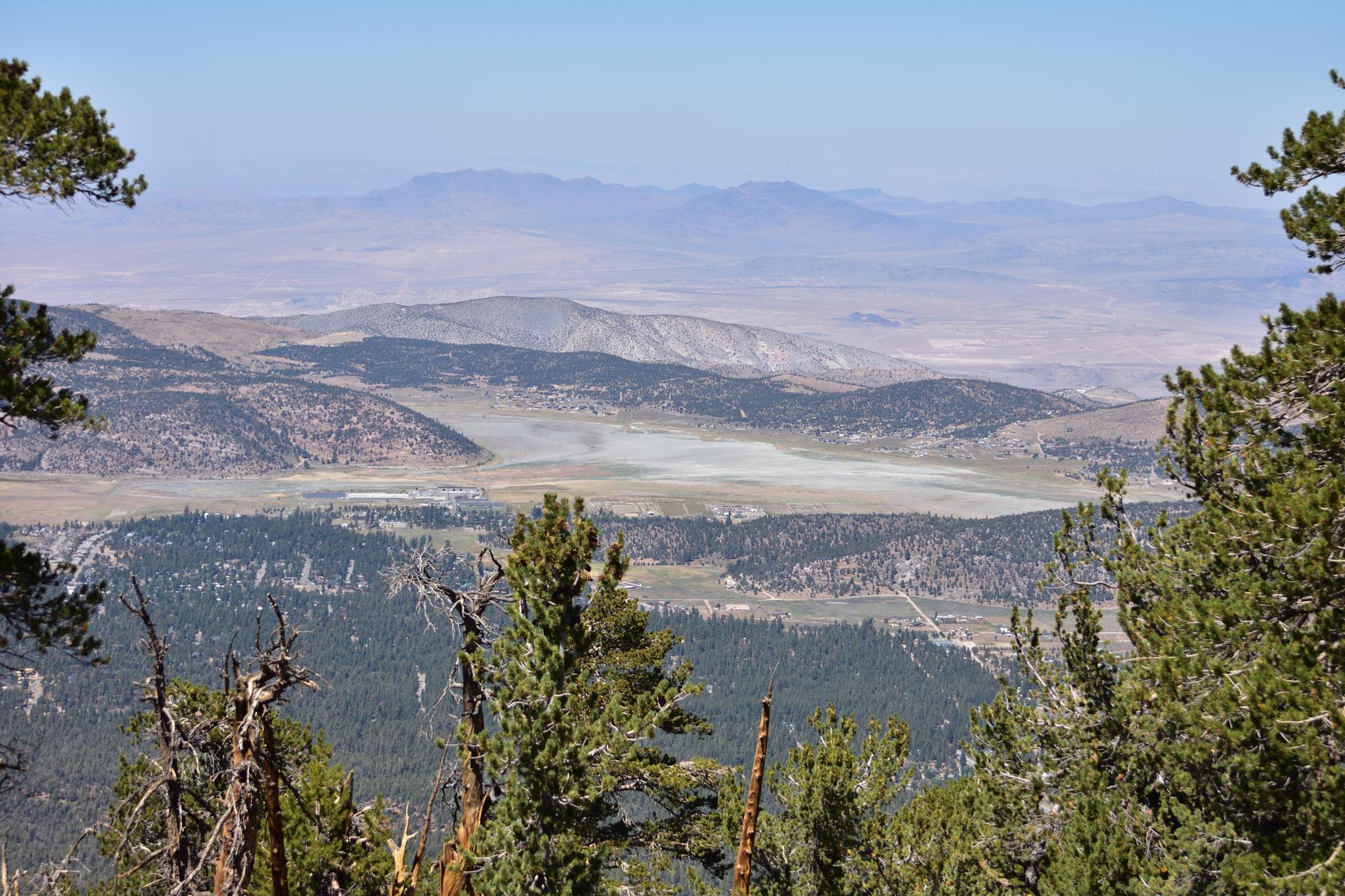 Hazy mountain vista with a wide valley and dry lakebed framed by trees.