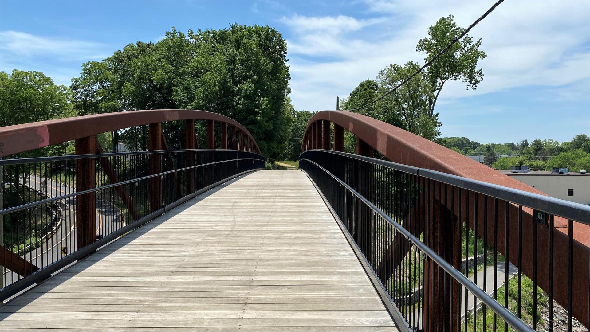 A modern wooden pedestrian bridge with dark metal railings under a blue sky.