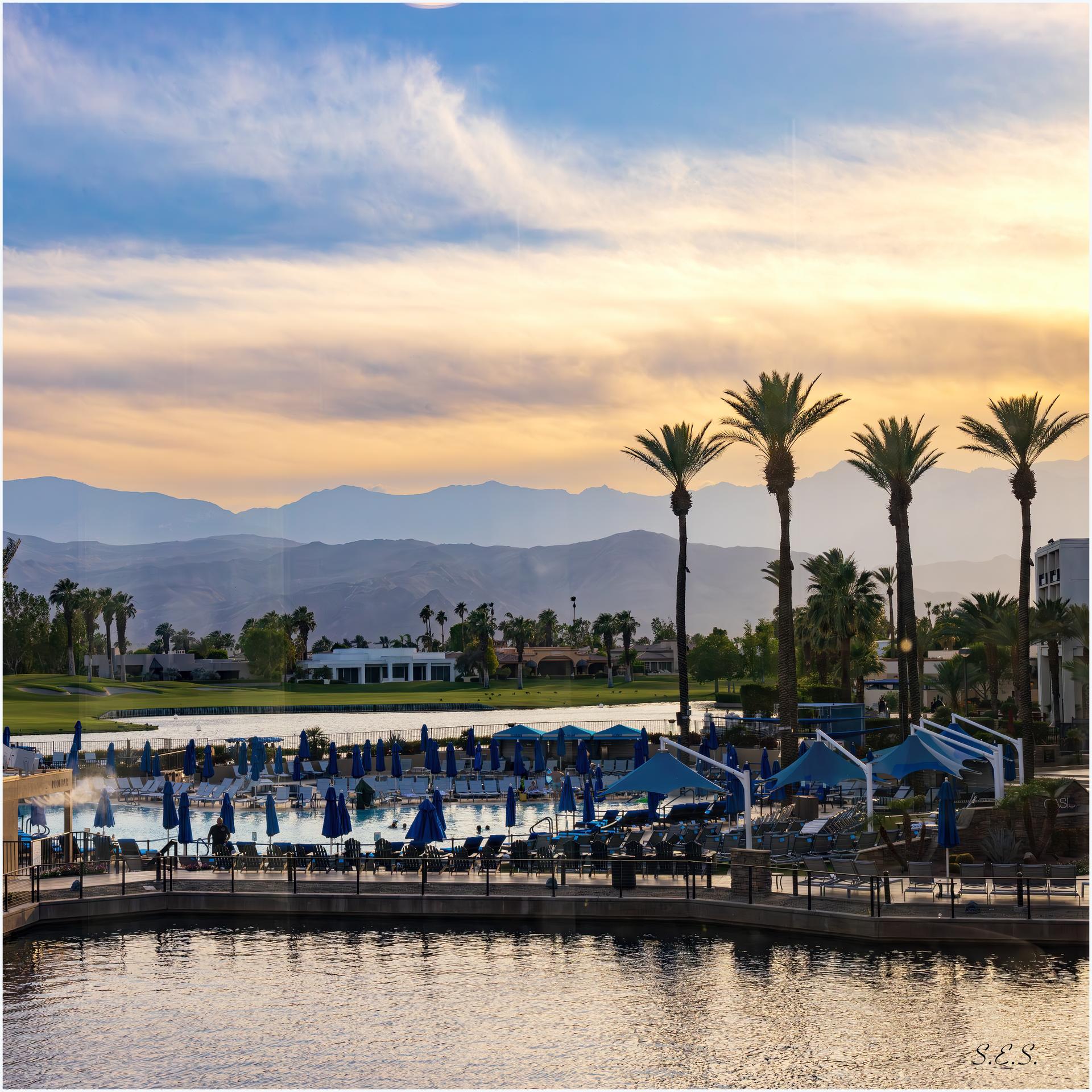Resort pool with palm trees and distant mountains at golden hour.