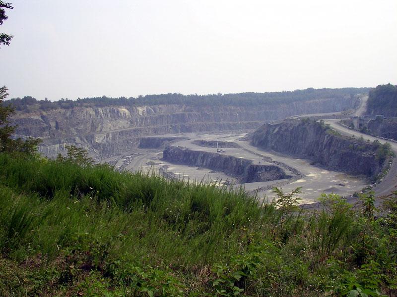 Expansive open-pit quarry with terraced rock walls and dirt roads under a hazy sky.
