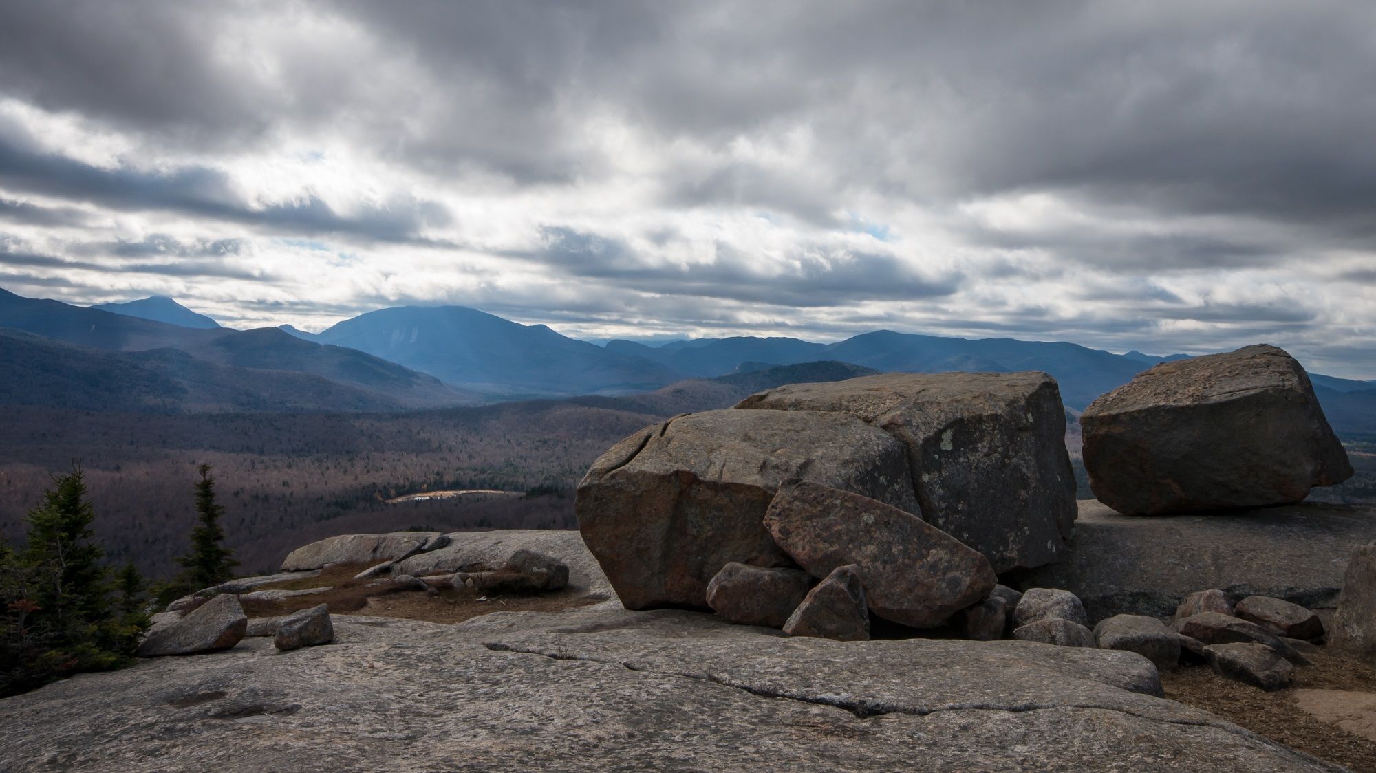 Large boulders on a rocky summit overlooking a vast mountain range under cloudy skies. - Pitchoff Mountain and Balanced Rocks Trail