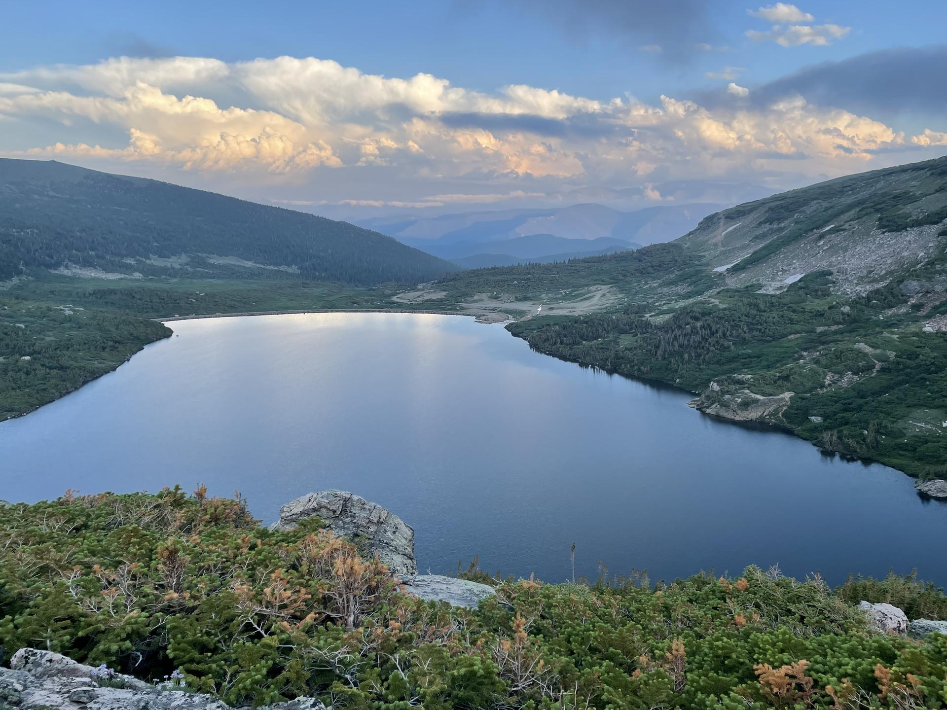 A serene mountain lake surrounded by green slopes under a cloudy sky.