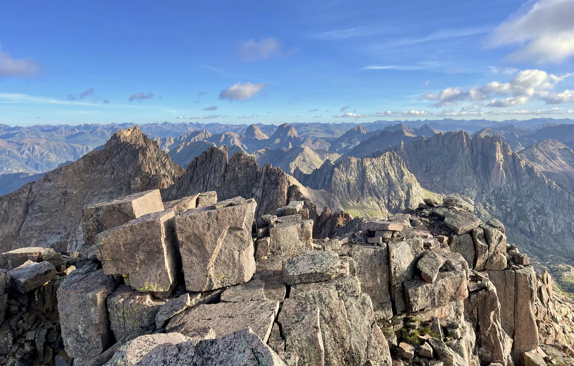Vast mountain range with rocky foreground under a bright blue sky.