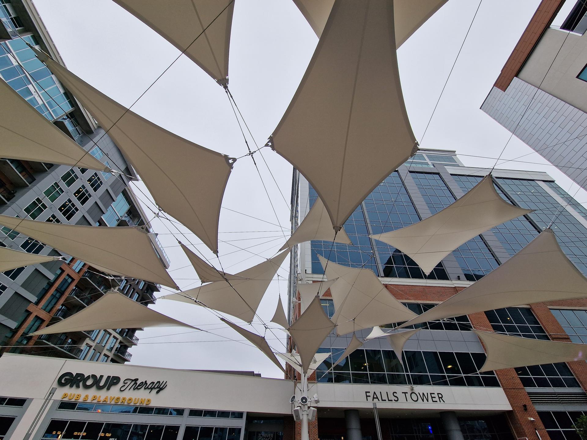 Abstract view of white shade sails against modern buildings and a cloudy sky.