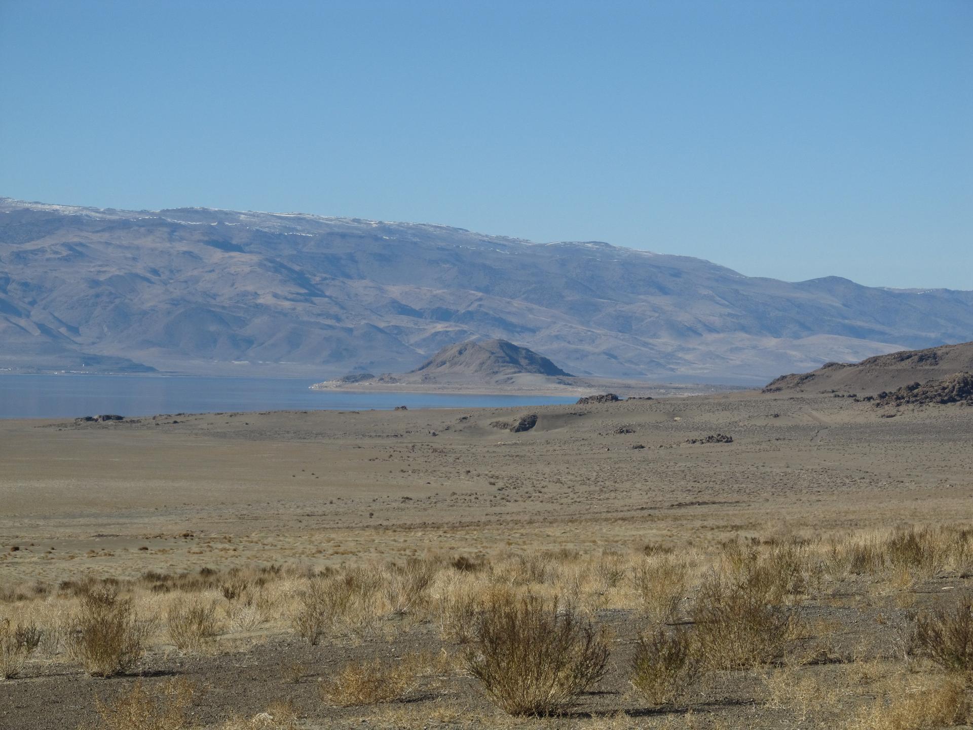 Expansive desert landscape with a large lake and snow-capped mountains under clear sky.