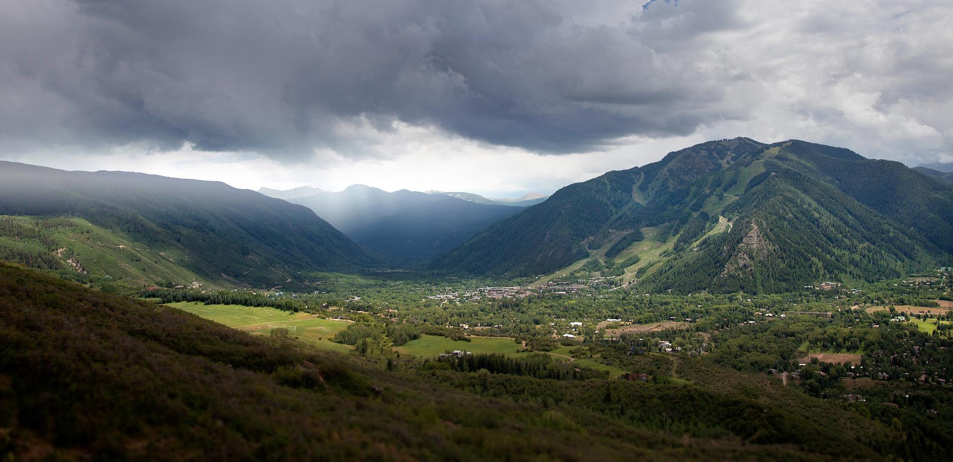 A vast green valley surrounded by mountains under a dramatic cloudy sky.