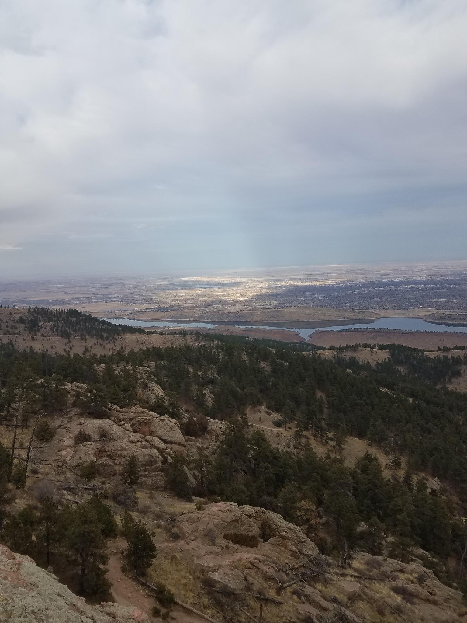 Overcast sky above a vast landscape with forests, rocky terrain, and distant water.