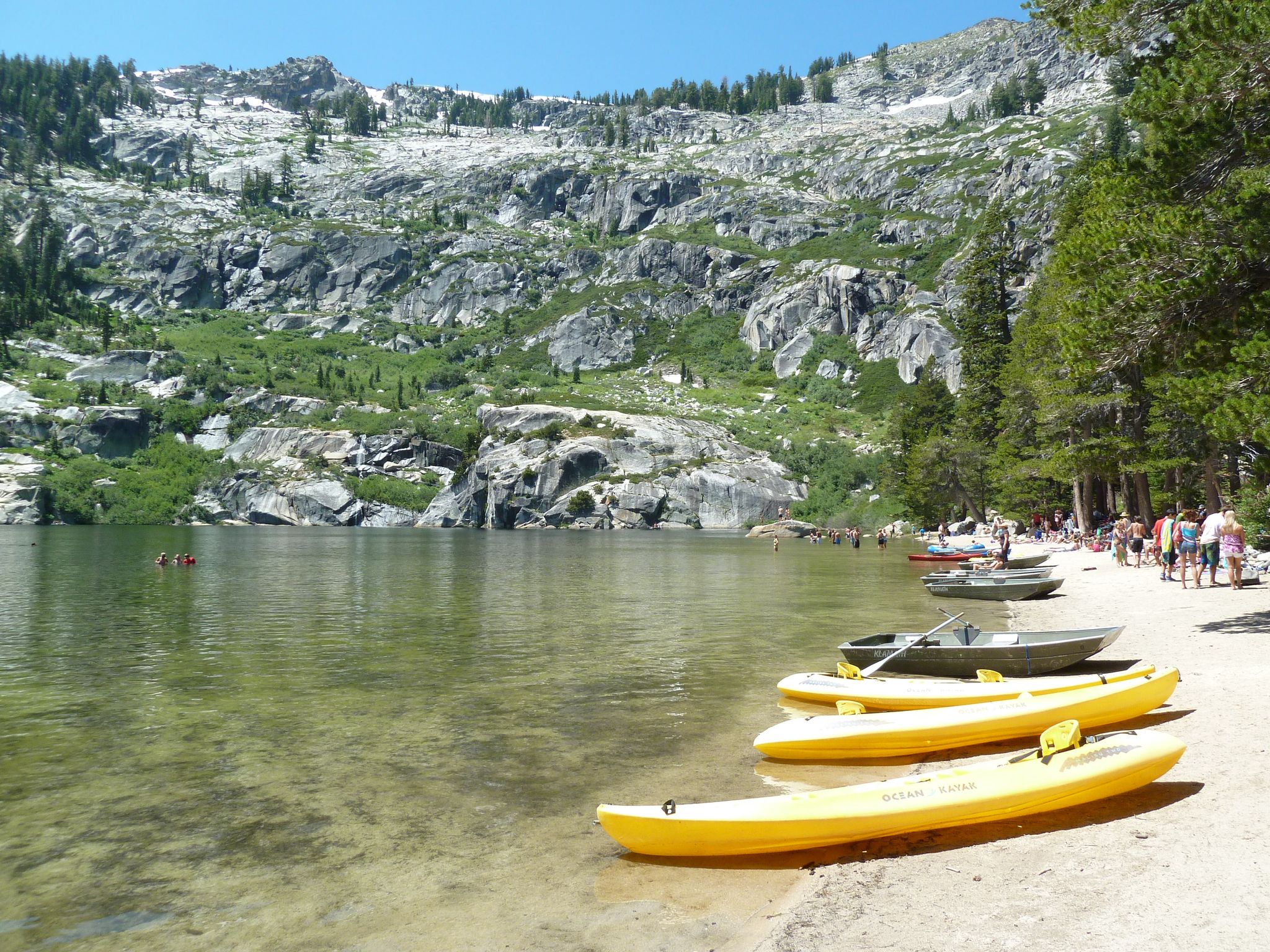 Sunny lake shore with yellow kayaks, people, and rocky mountains. - Angora Ridge Trail