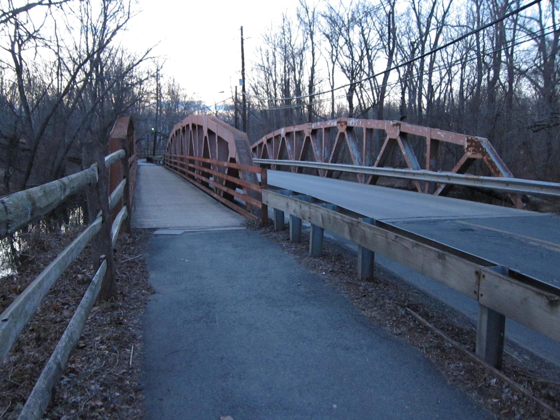 Two bridges, one pedestrian and one vehicle, over water at dusk.