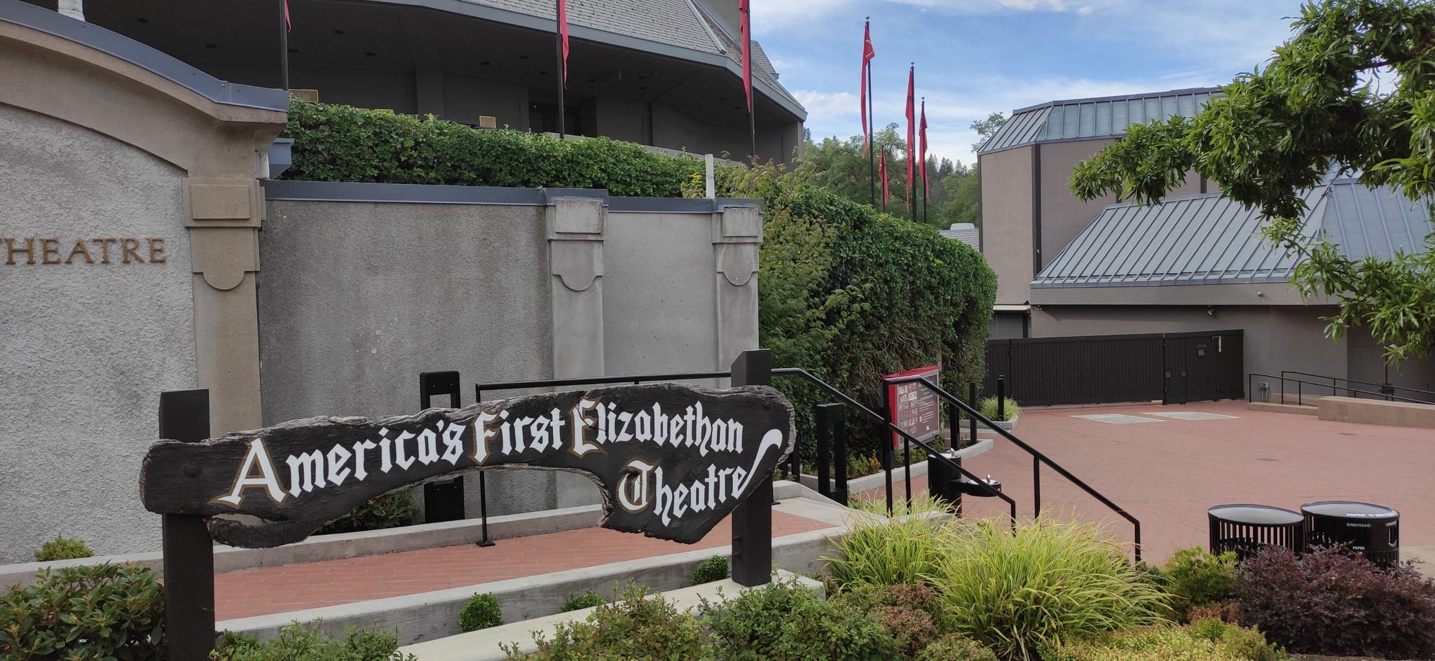 A sign for a theater in front of a large building with red flags.