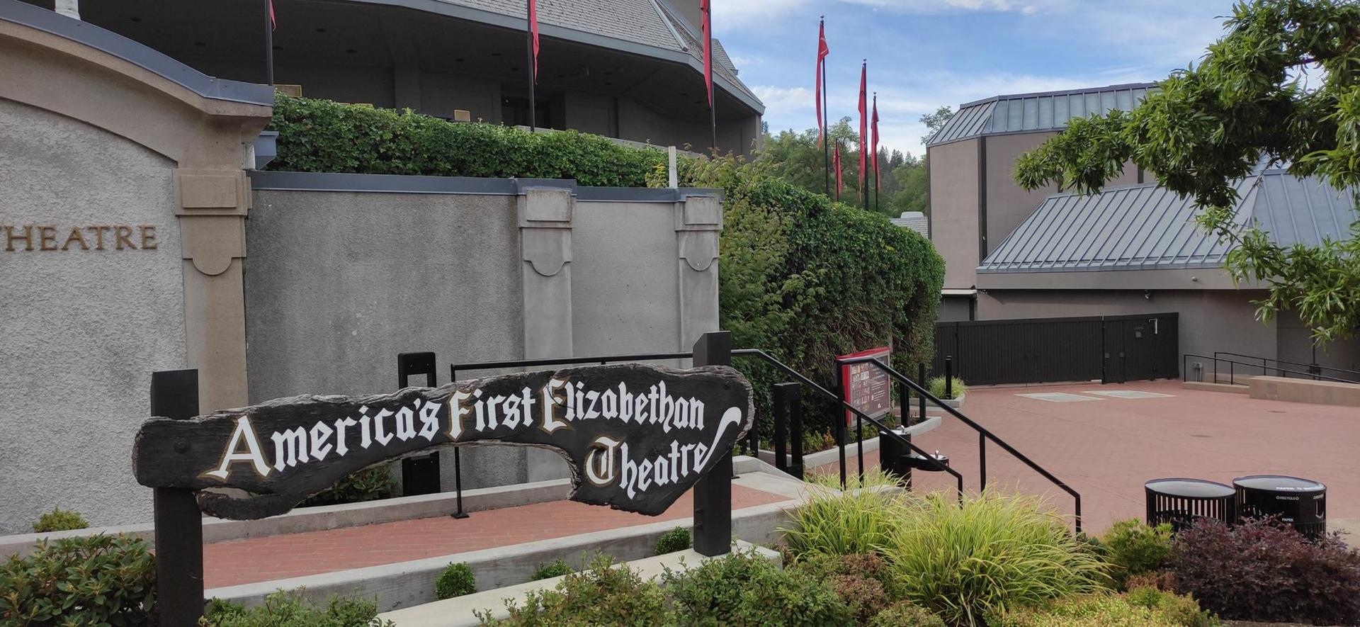 A sign for a theater in front of a large building with red flags.