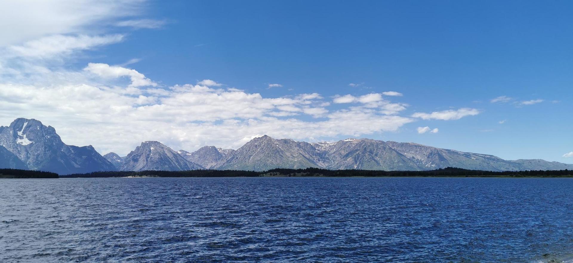 Wide lake with distant mountains under a bright blue sky.