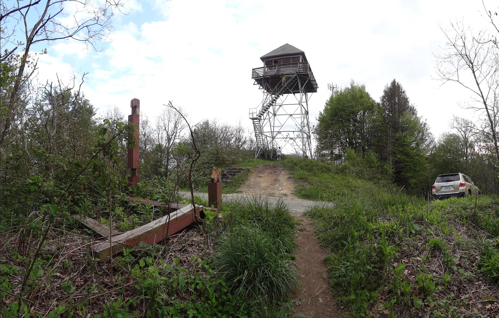 A fire lookout tower stands on a grassy hill with a car nearby.