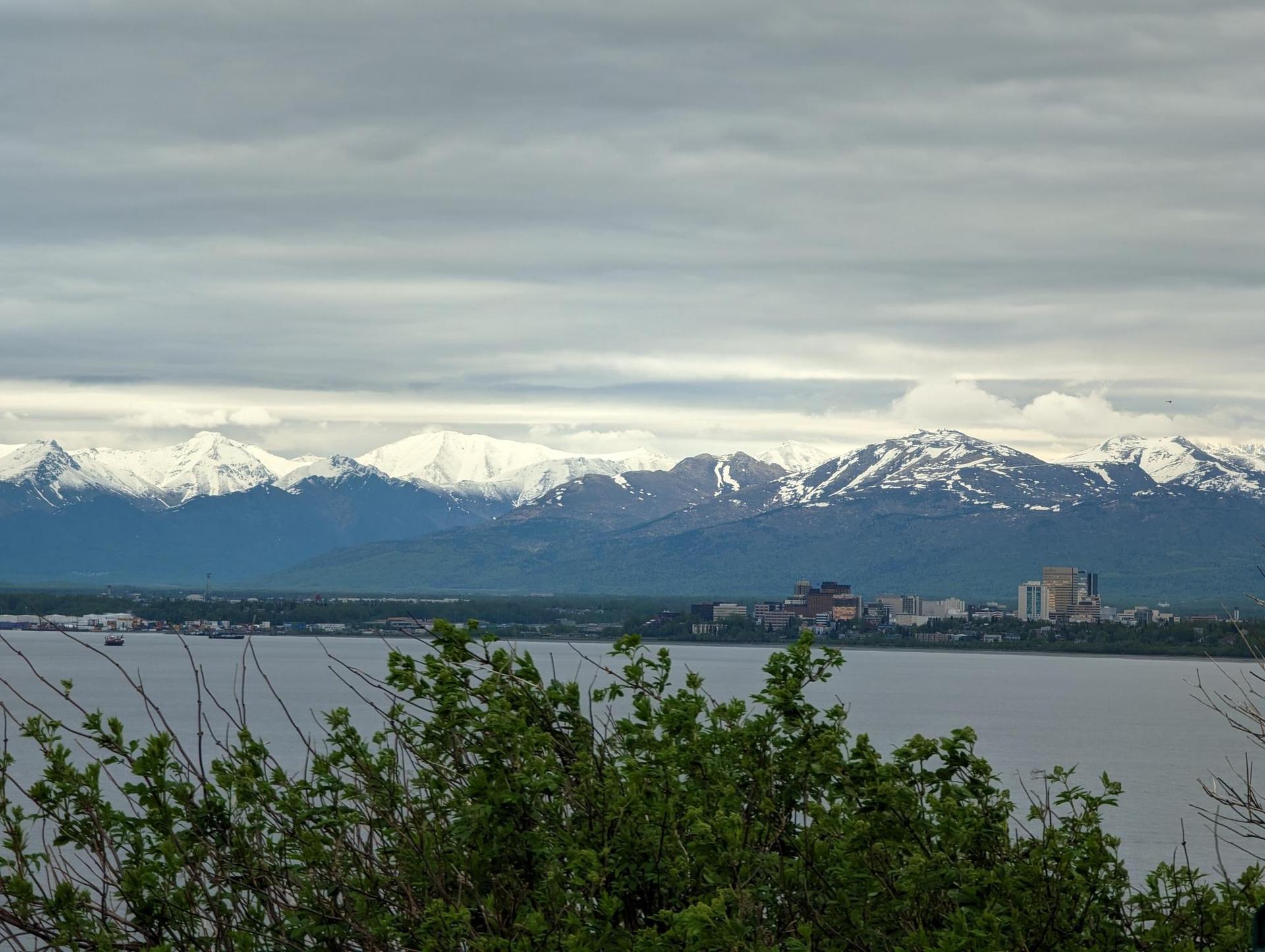 City skyline by a large body of water, backed by snow-capped mountains.