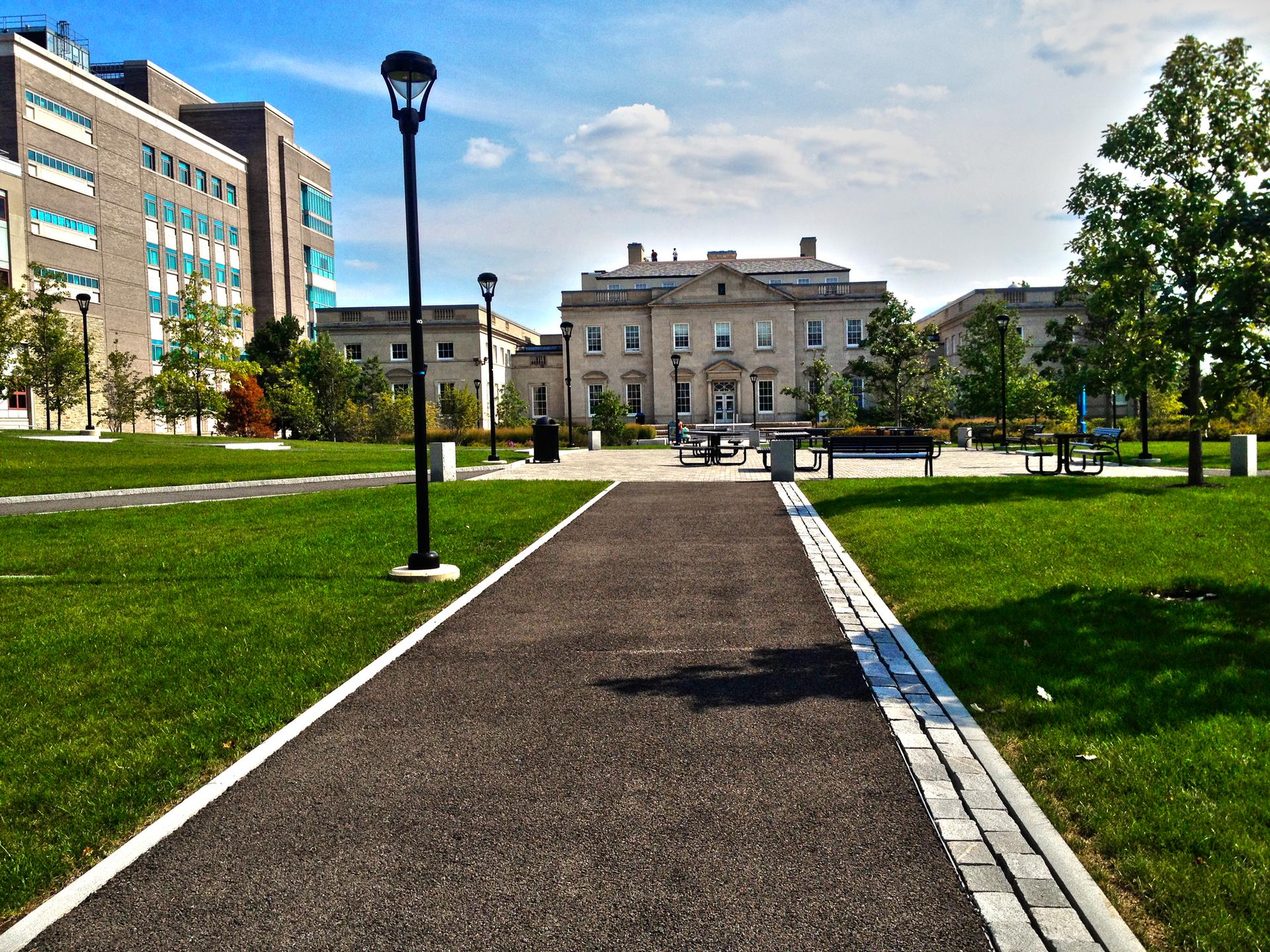 A paved path through green lawns leads to a grand building on a sunny day.