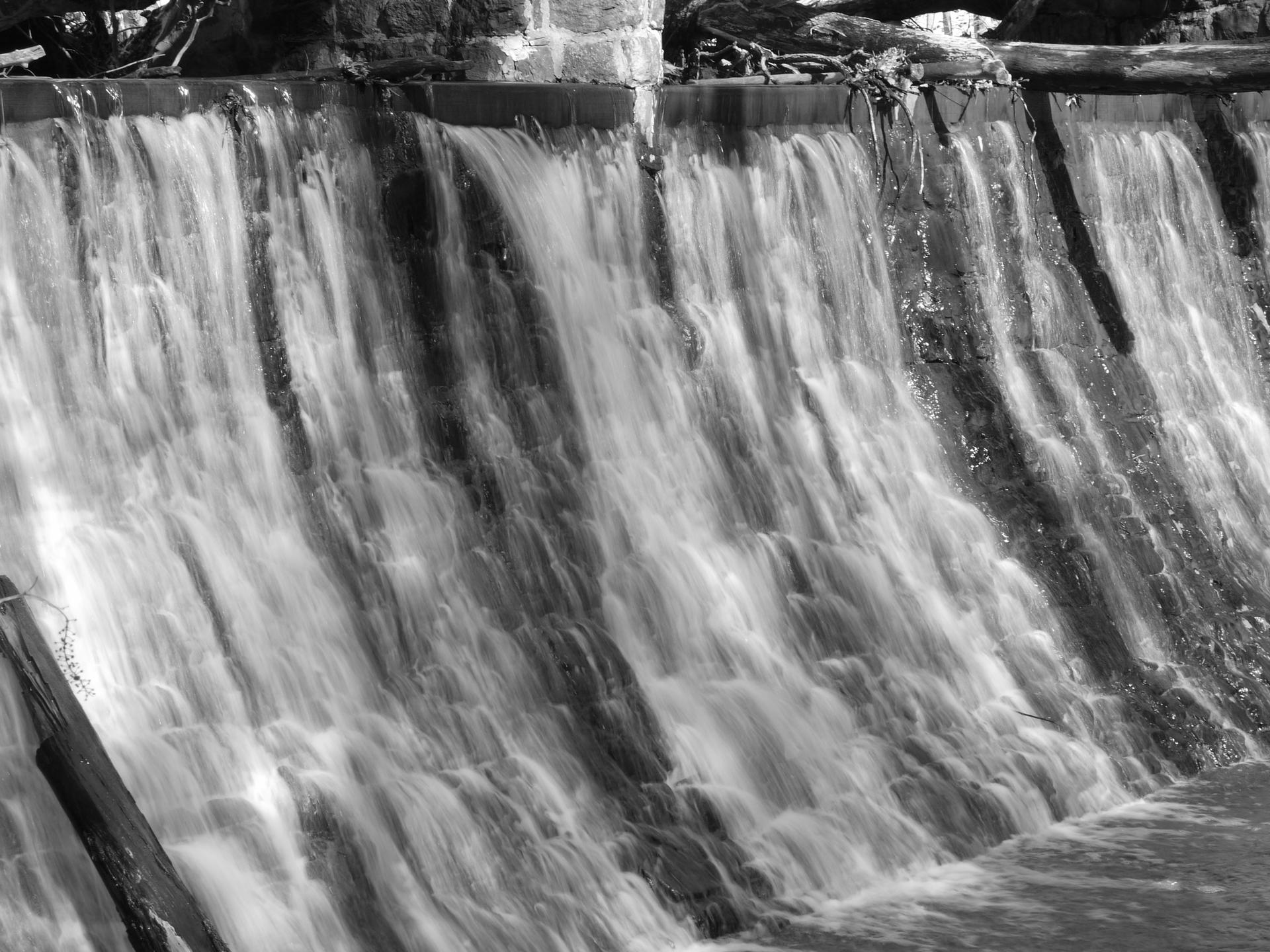 Black and white image of water cascading over a man-made dam.