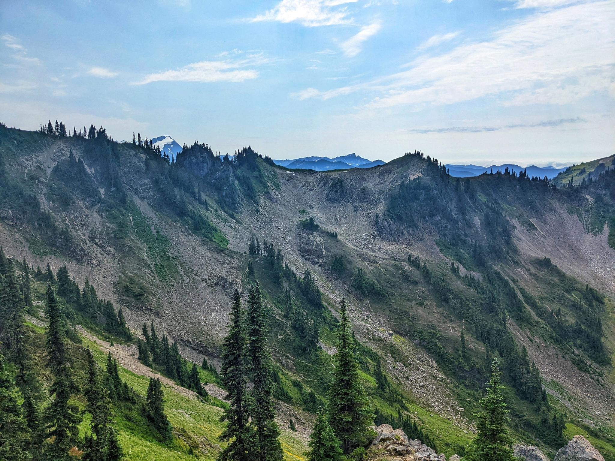 Steep, green and rocky mountain slopes under a bright, cloudy sky.