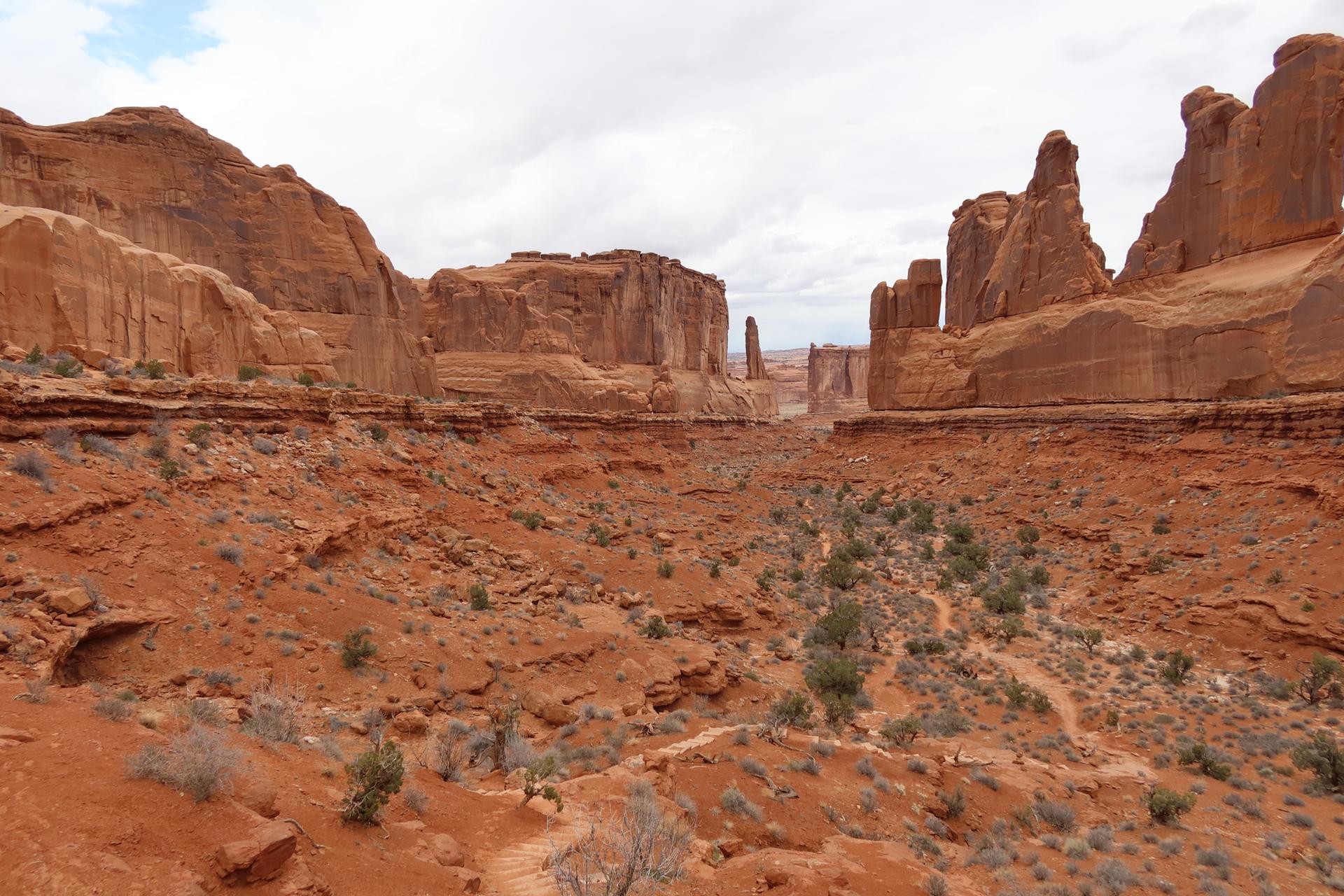 Wide view of a red desert valley with distant rock formations.