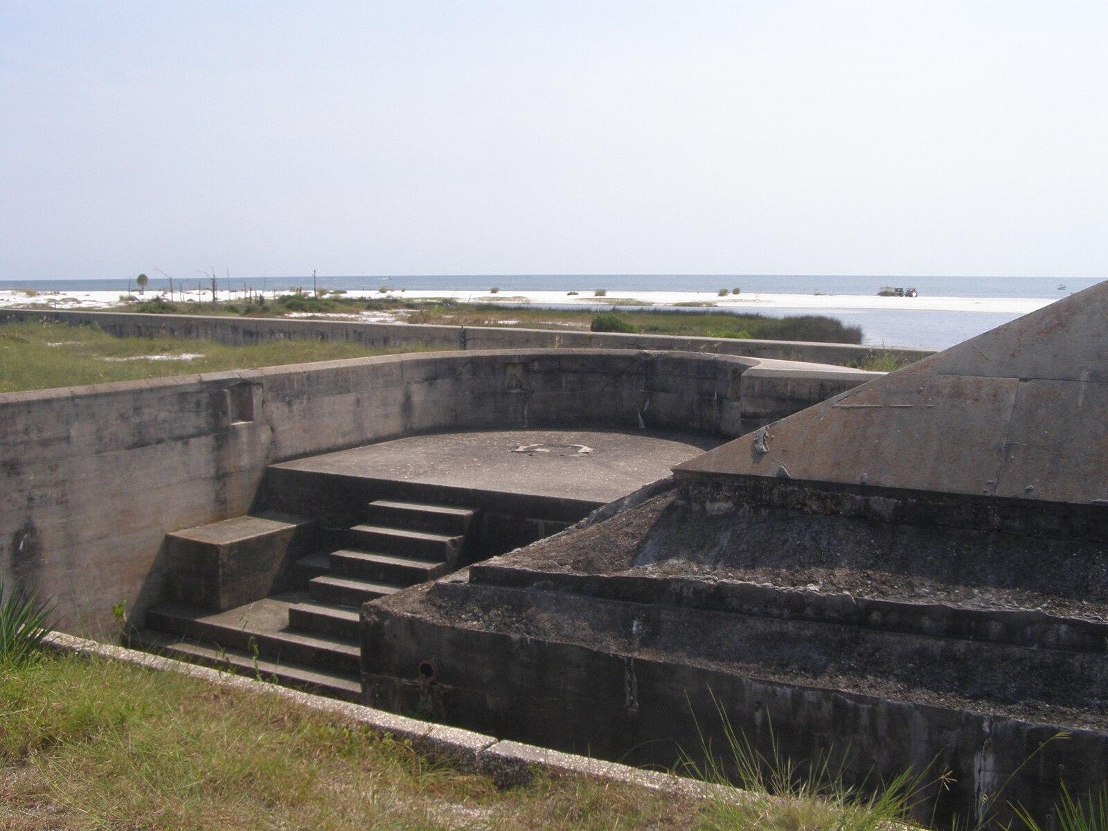 Concrete bunker with steps overlooking a sunny ocean and sandy shore.