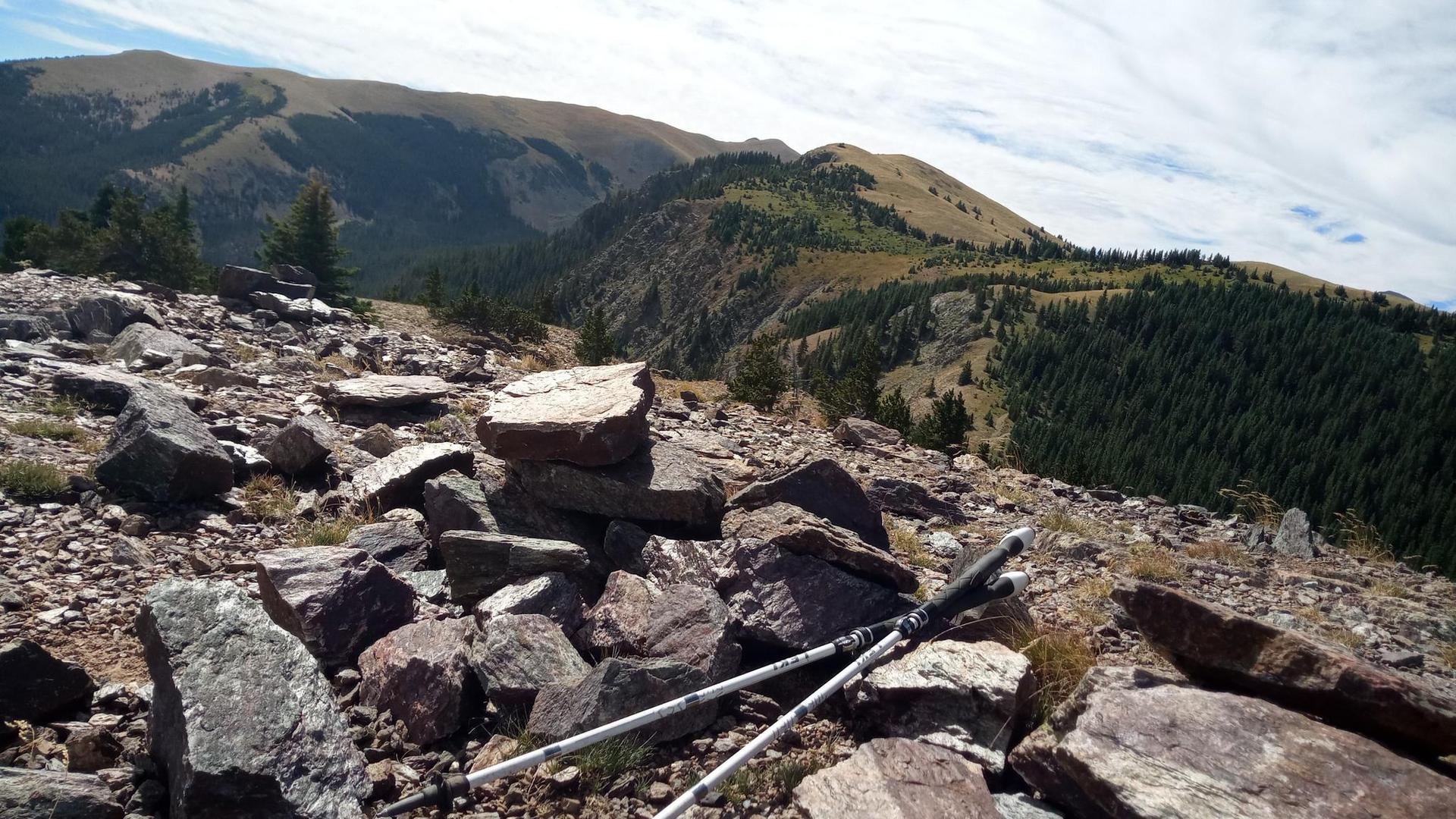 Hiking poles rest on a rocky mountain peak overlooking forested valleys.