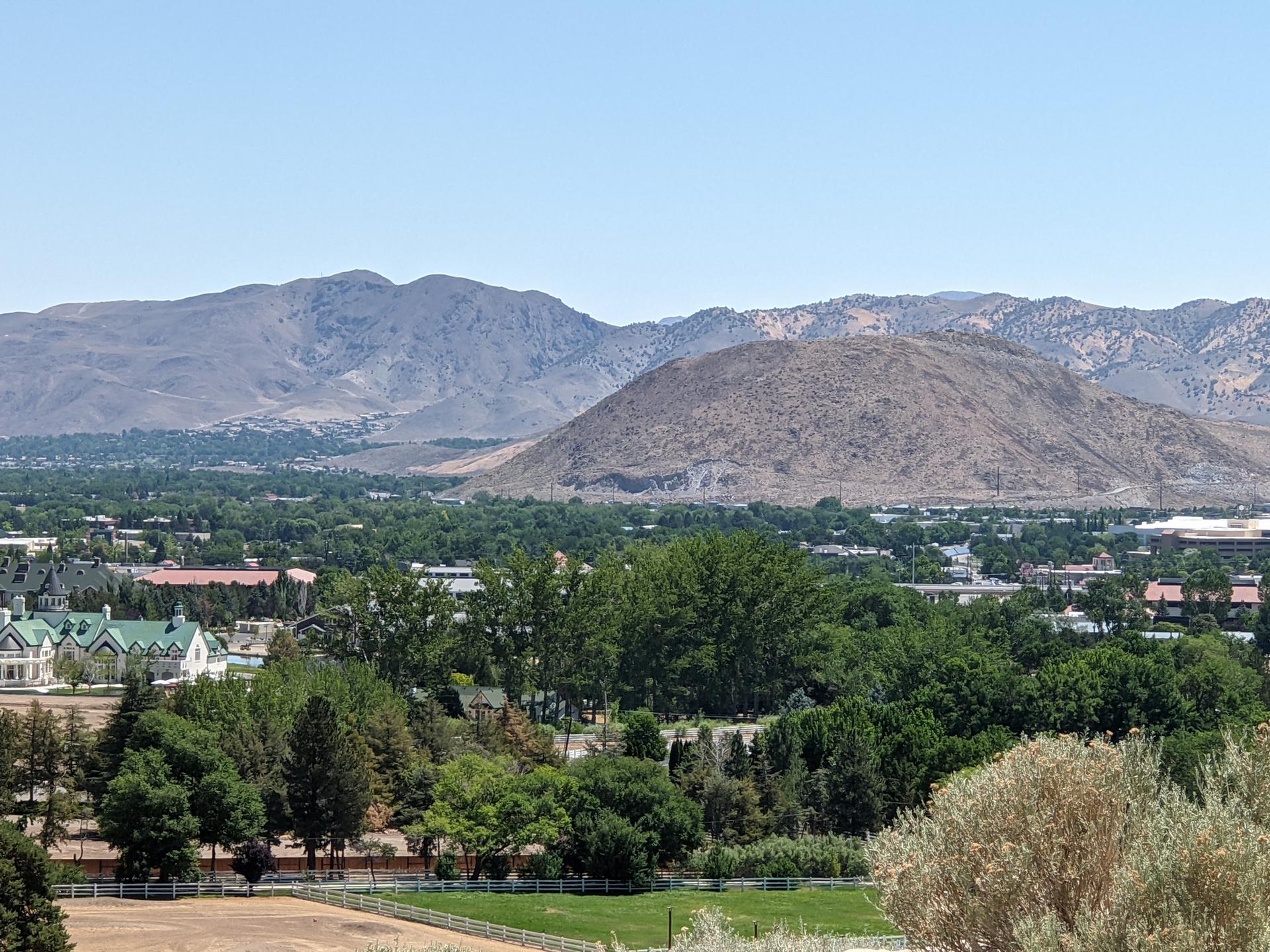 A panoramic view of a town nestled among green trees and distant mountains.