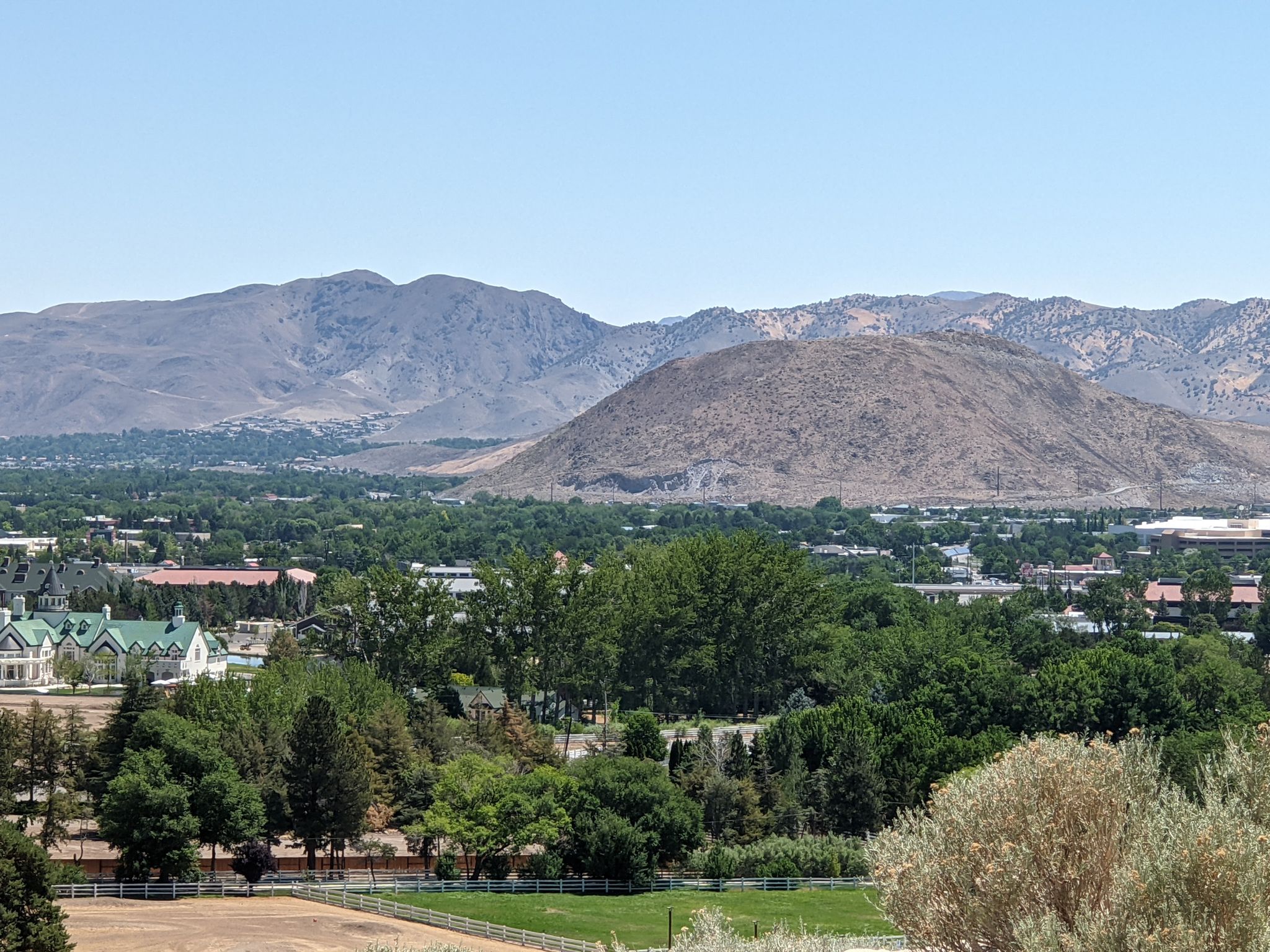 A panoramic view of a town nestled among green trees and distant mountains. - Reno's Southeast Highlight Loop