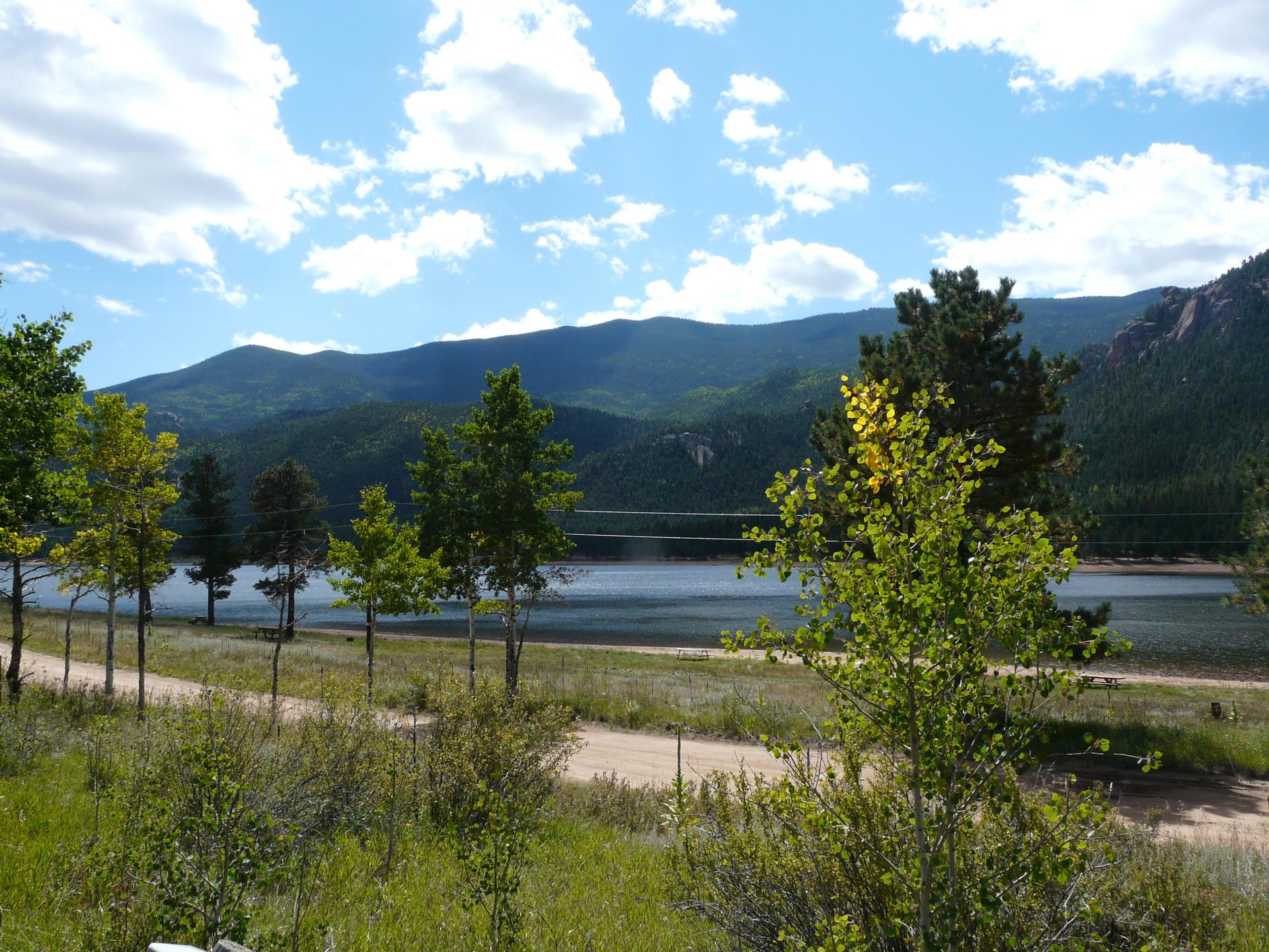Bright sunny day over a calm lake, distant mountains, and green trees.