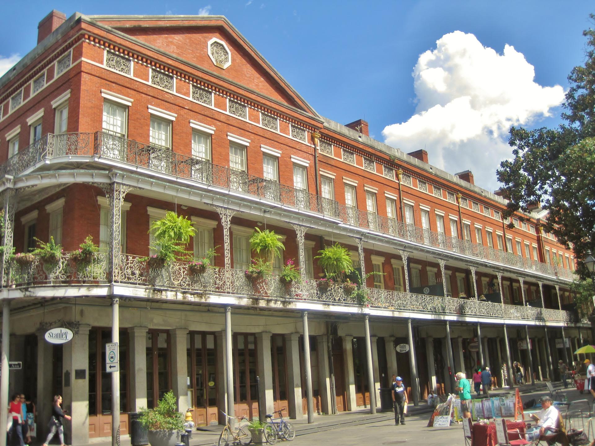 A historic brick building with ornate balconies overlooks a busy street with people.
