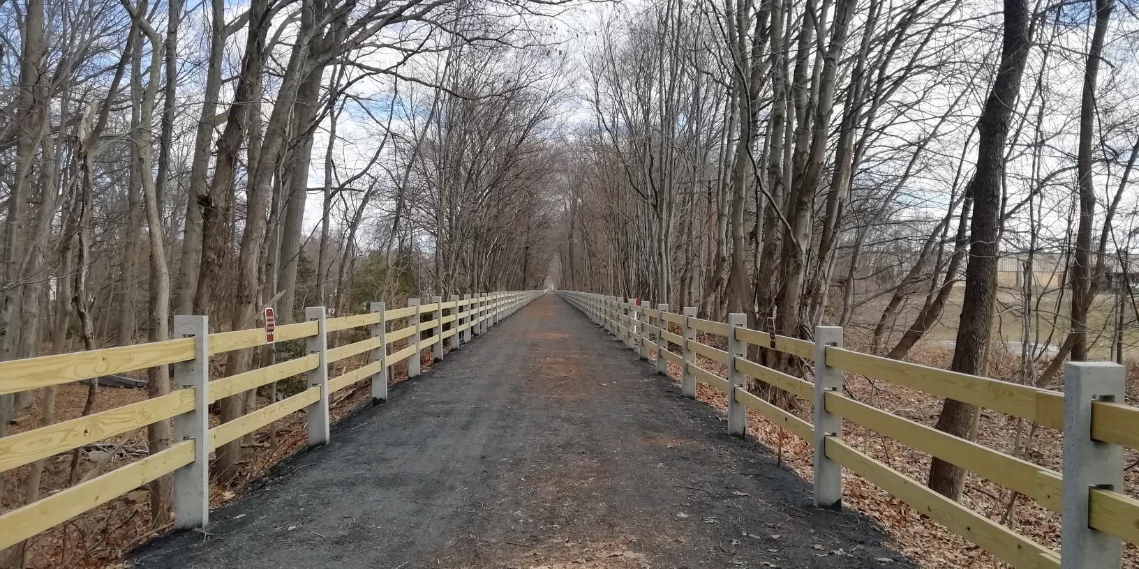 Long gravel path lined with wooden fences, surrounded by bare trees.