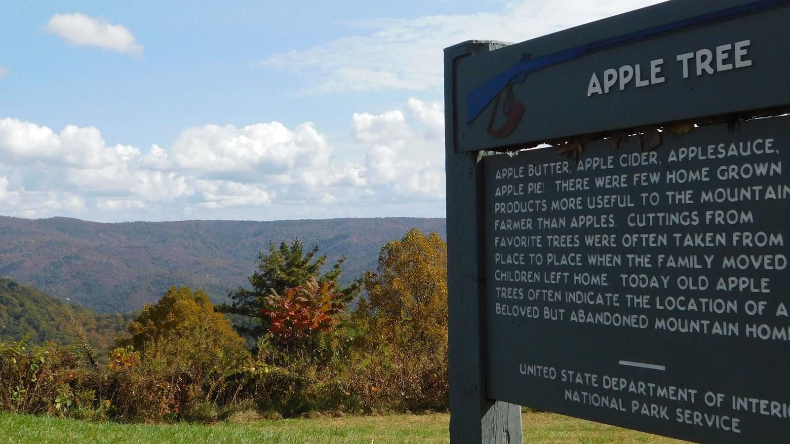 Informational sign beside a scenic view of forested mountains under a partly cloudy sky.