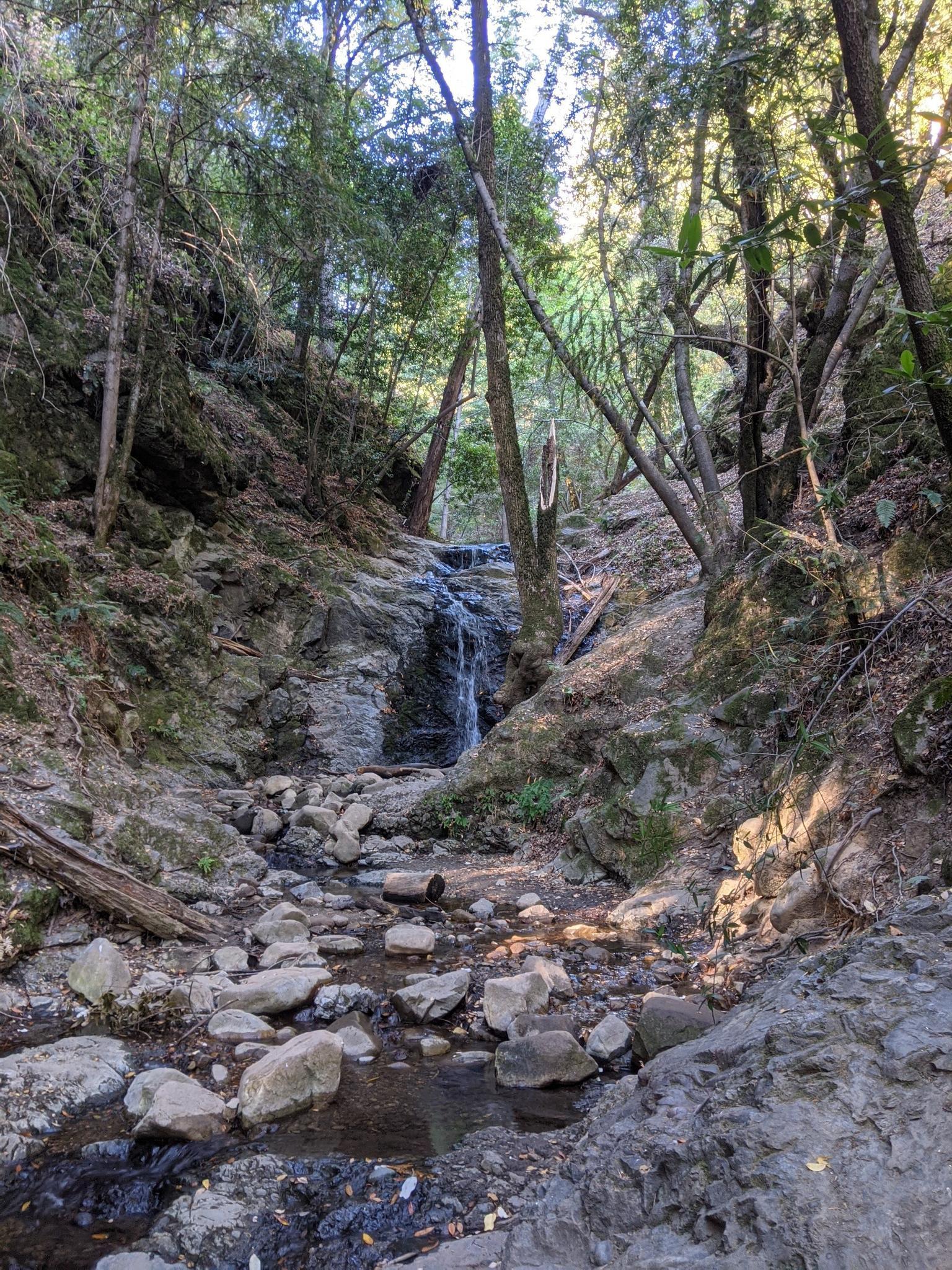 Small waterfall flowing over rocks in a shaded, rocky stream bed.