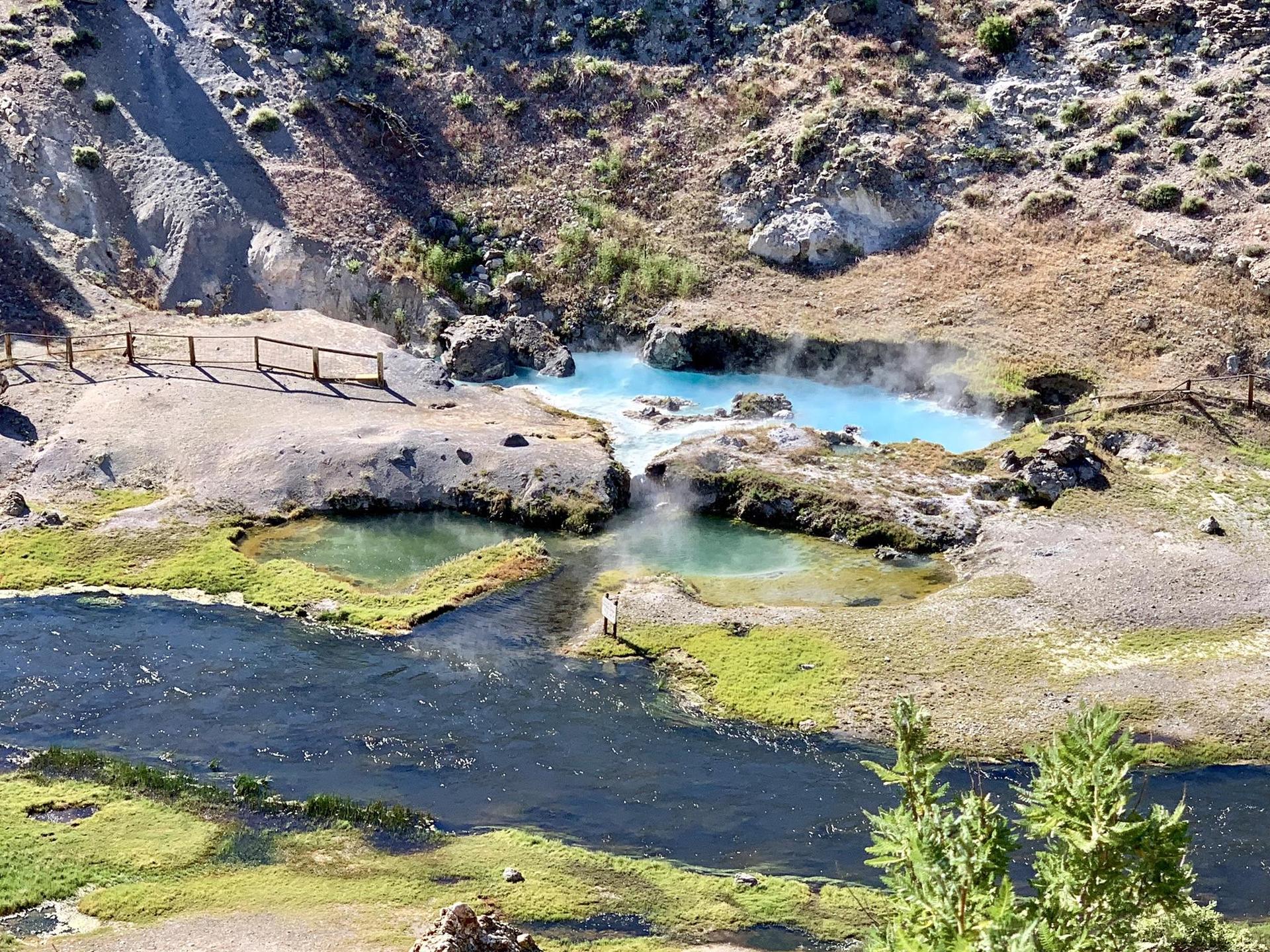 Close-up of a river, green banks, and steaming blue hot springs.
